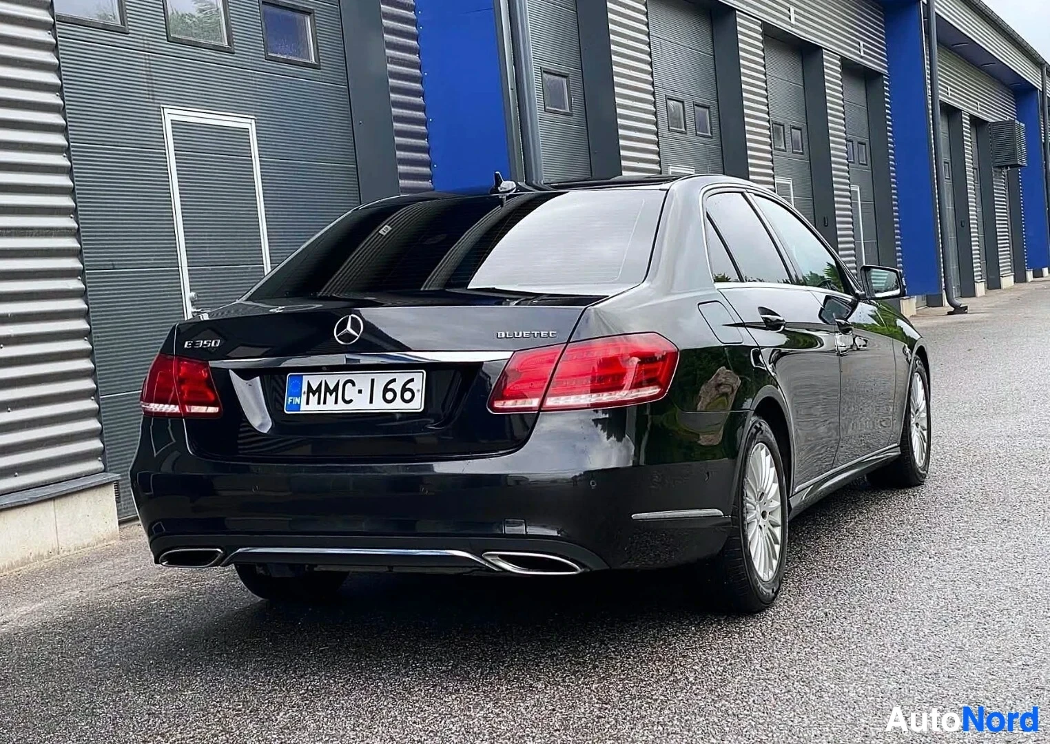 Takaviisto: Musta Mercedes-Benz E-sarjan sedan takavasemmalta näkymä, rekisterikilpi MMC·I66, takaluukulla E350 ja BlueTec -merkinnät
