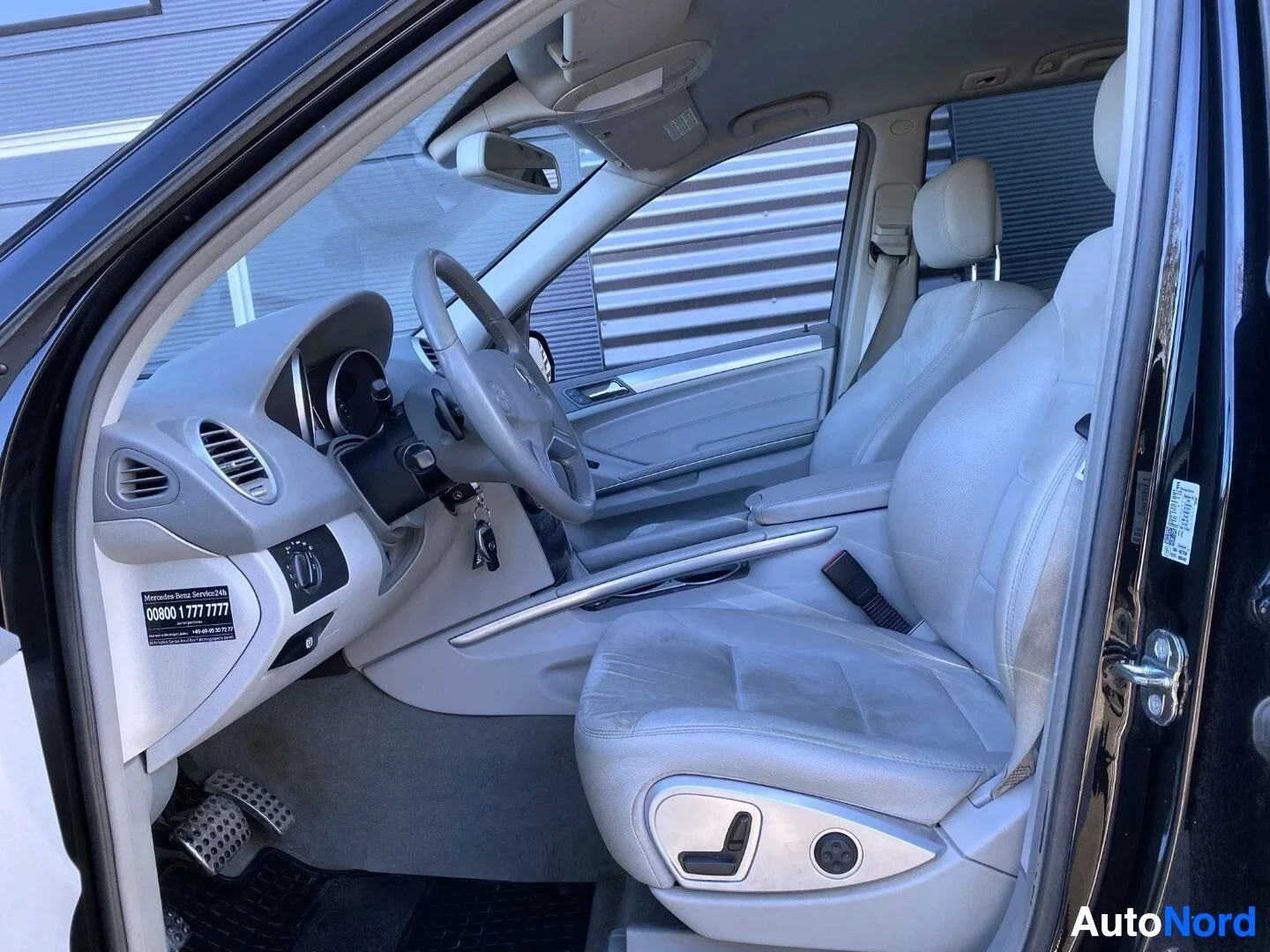 Etuistuimet: Auton etupihan sisäpuoli, näkyvissä Mercedes-merkkinen ohjauspyörä, valkoiset nahkaistuimet, harmaa kojelauta ja kuljettajan istuimen säädöt ovessa. Ohjauspyörä