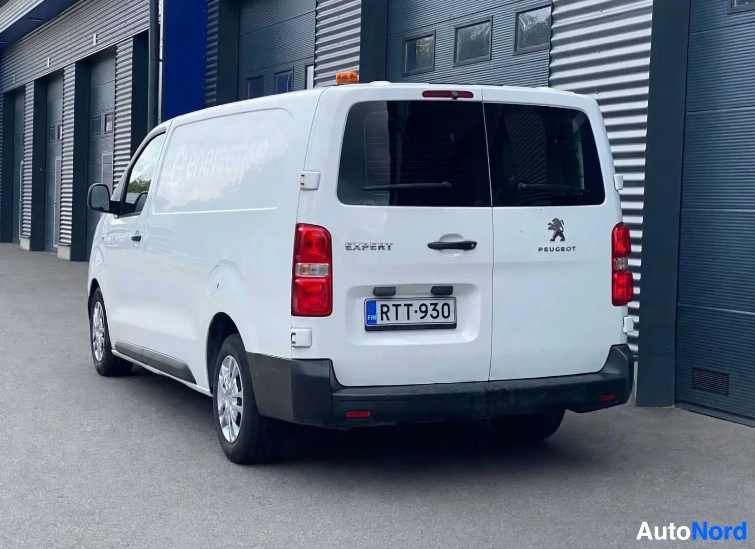 Takaviisto: Valkoinen pakettiauto, jonka takaosassa on musta puskuri, mustat peilit ja oranssi majakkavalo katolla. Rekisterikilpi on