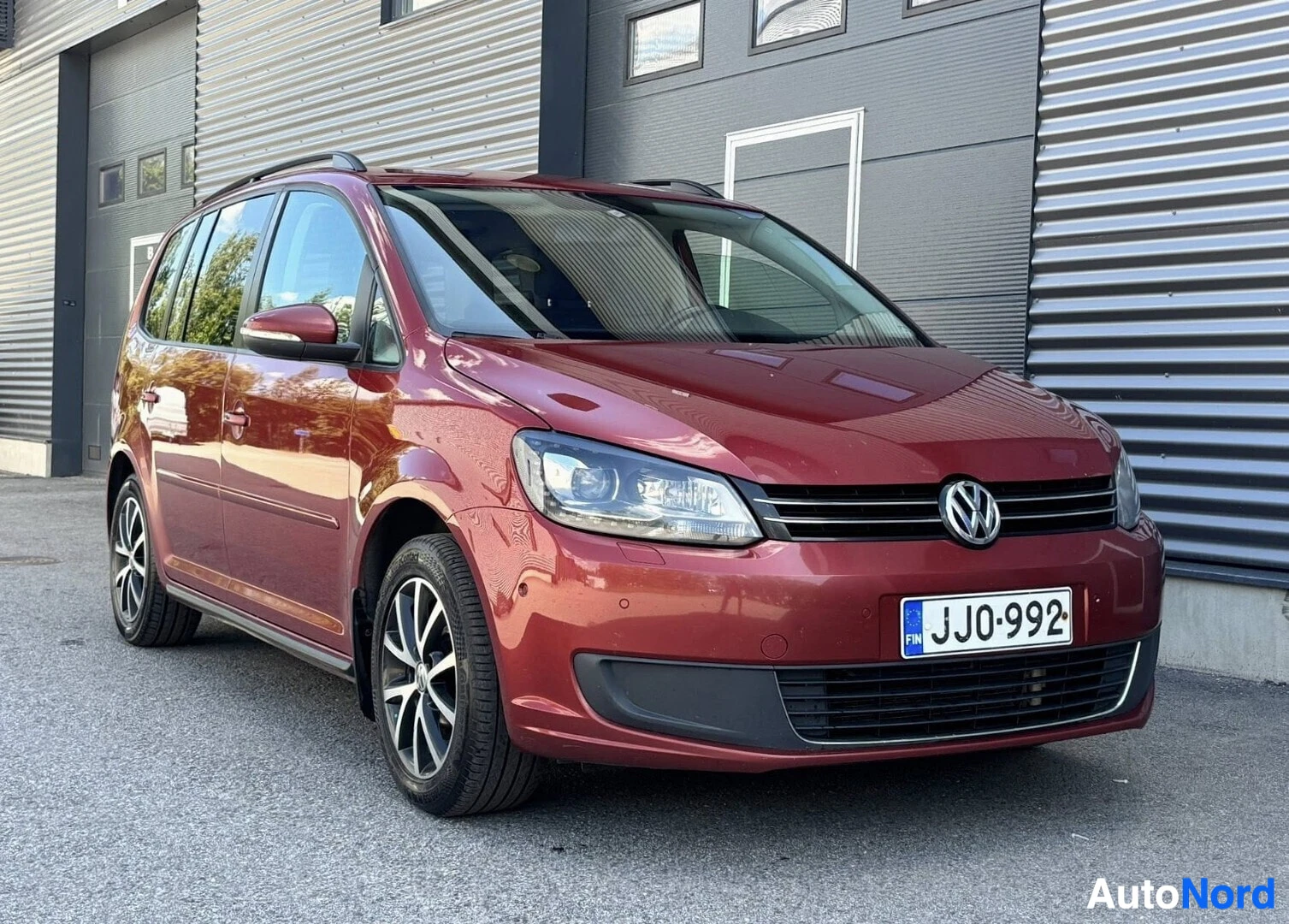 Etuviisto, nokka oikealle: Punainen Volkswagen Touran etupuolelta kuvattuna, oikealle kallistuneella kameralla. Rekisterinumero näkyy