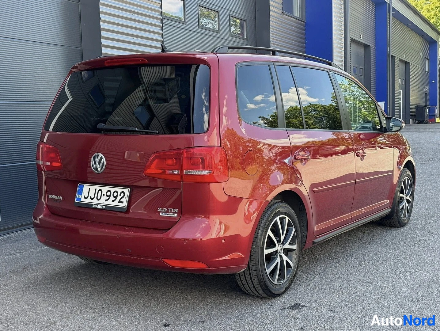 Takaa: Punainen Volkswagen Touran takaa kuvattuna. Rekisterinumero, tekstit "TOURAN" ja "2.0 TDI" näkyvät takaovet alareunassa