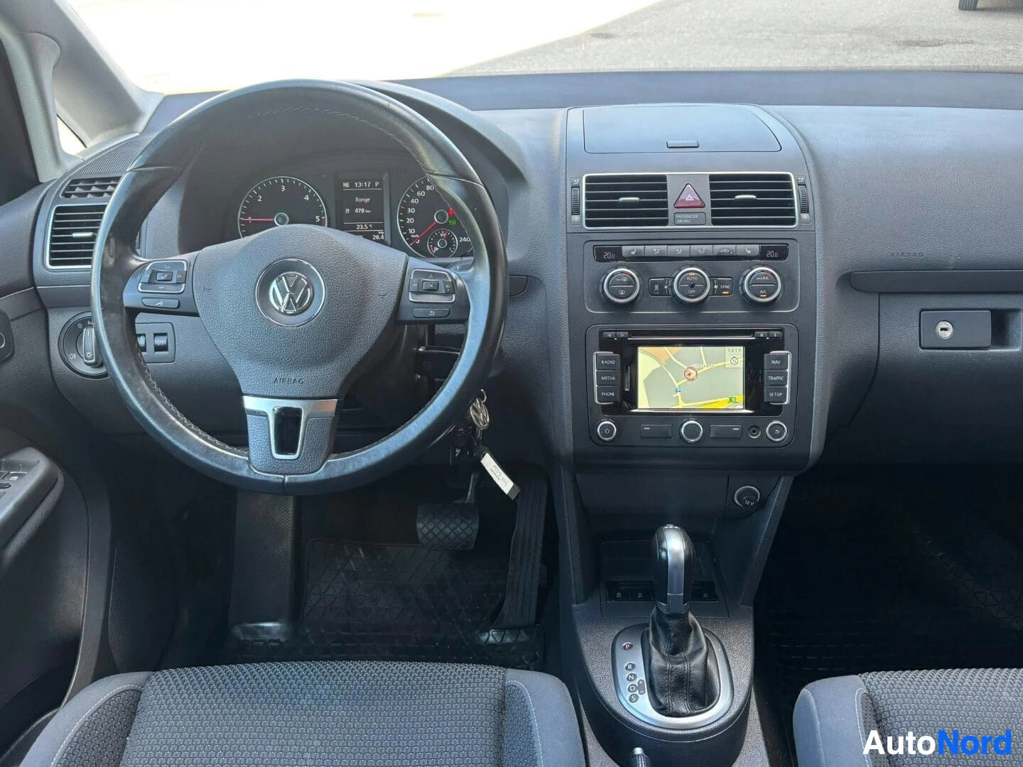 Ohjaamo: Auton ohjaamo suoraan edestä kuvattuna. Ohjauspyörässä Volkswagen-logo. Instrumenttipaneeli näkyy, keskellä navigointijärjestelmä kartalla. Keskikonsoli ilmasto