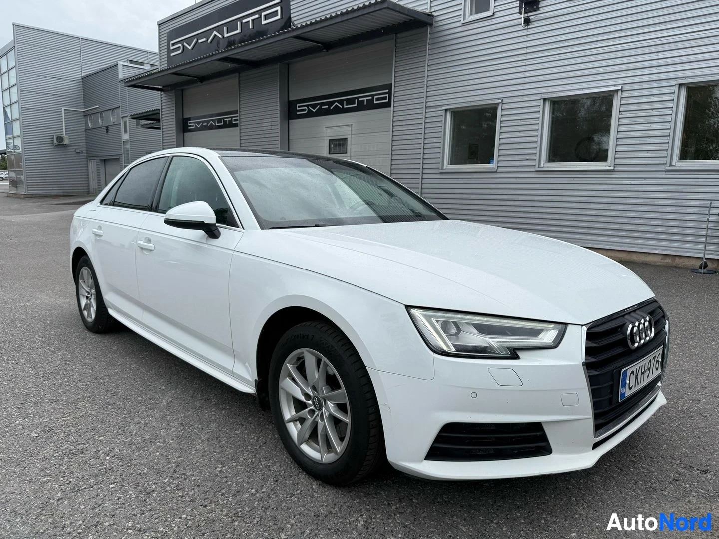 Etuviisto, nokka oikealle: Valkoinen Audi A4 sedan, kuvattu kolmen neljänneksen kulmasta oikealta, pysäköitynä SV-AUTO-liikkeen edustalla.