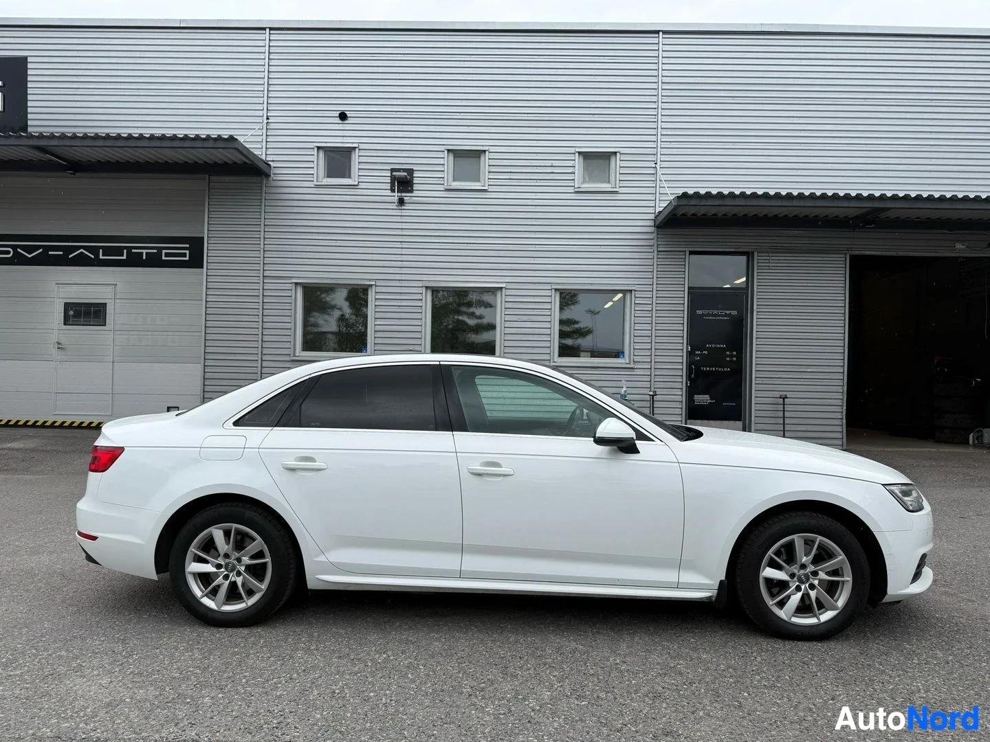 Sivulta: Valkoinen Audi A4 sedan, kuvattu sivulta oikealle päin, pysäköitynä SV-AUTO-liikkeen edessä.