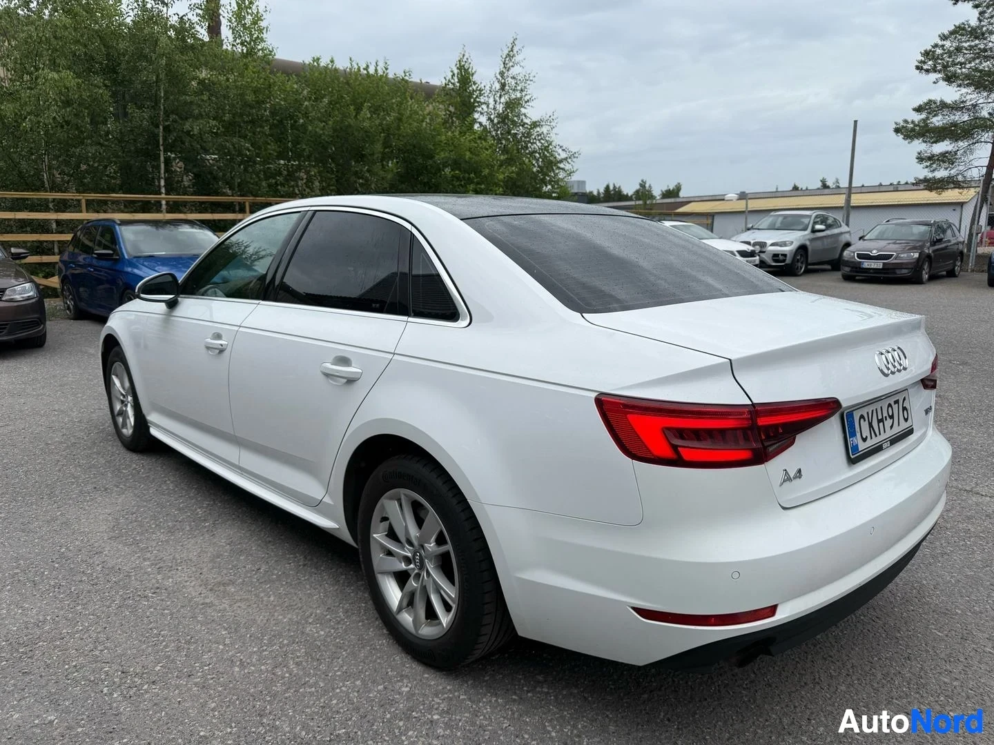 Takaviisto: Valkoinen Audi A4 sedan sivusta ja takaapäin kuvattuna oikealle. Neljä ovea näkyvät. Rekisterikilpi näkyy