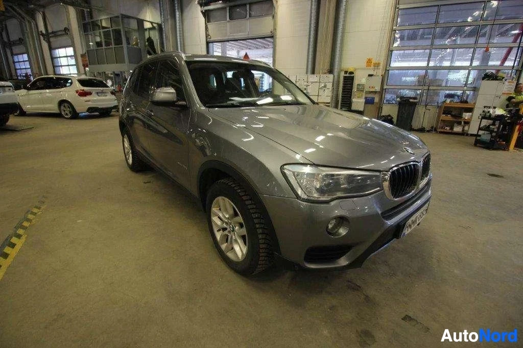 Etuviisto, nokka oikealle: Harmaa BMW X3 -maastoauto kylmässä varastohallissa, etupuoli ja vasen sivu näkyvissä, nosta-ovi auki