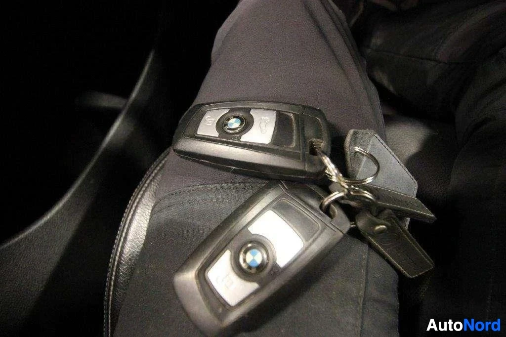Yksityiskohta: Kaksi BMW-avaintetta, joissa on tunnettu BMW-logo, päälle asetettu harmaan värisen ajoasun päälle