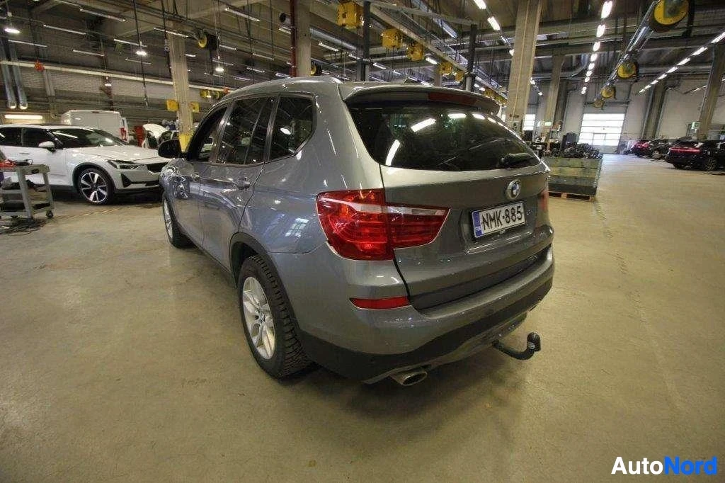 Takaviisto: Harmaa BMW X3 -maastoauto varastohallissa, takaosa ja oikea sivu näkyvissä, rekisterikilvessä NMK993, vetokoukku näkyvissä
