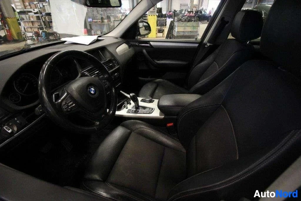 Etuistuimet: Auton sisäosa sivusta, musta nahkainen istuinta vasemmalla, musta nahkapenkki, BMW-ratti vasemmalla, harmaa keskuspaneeli.