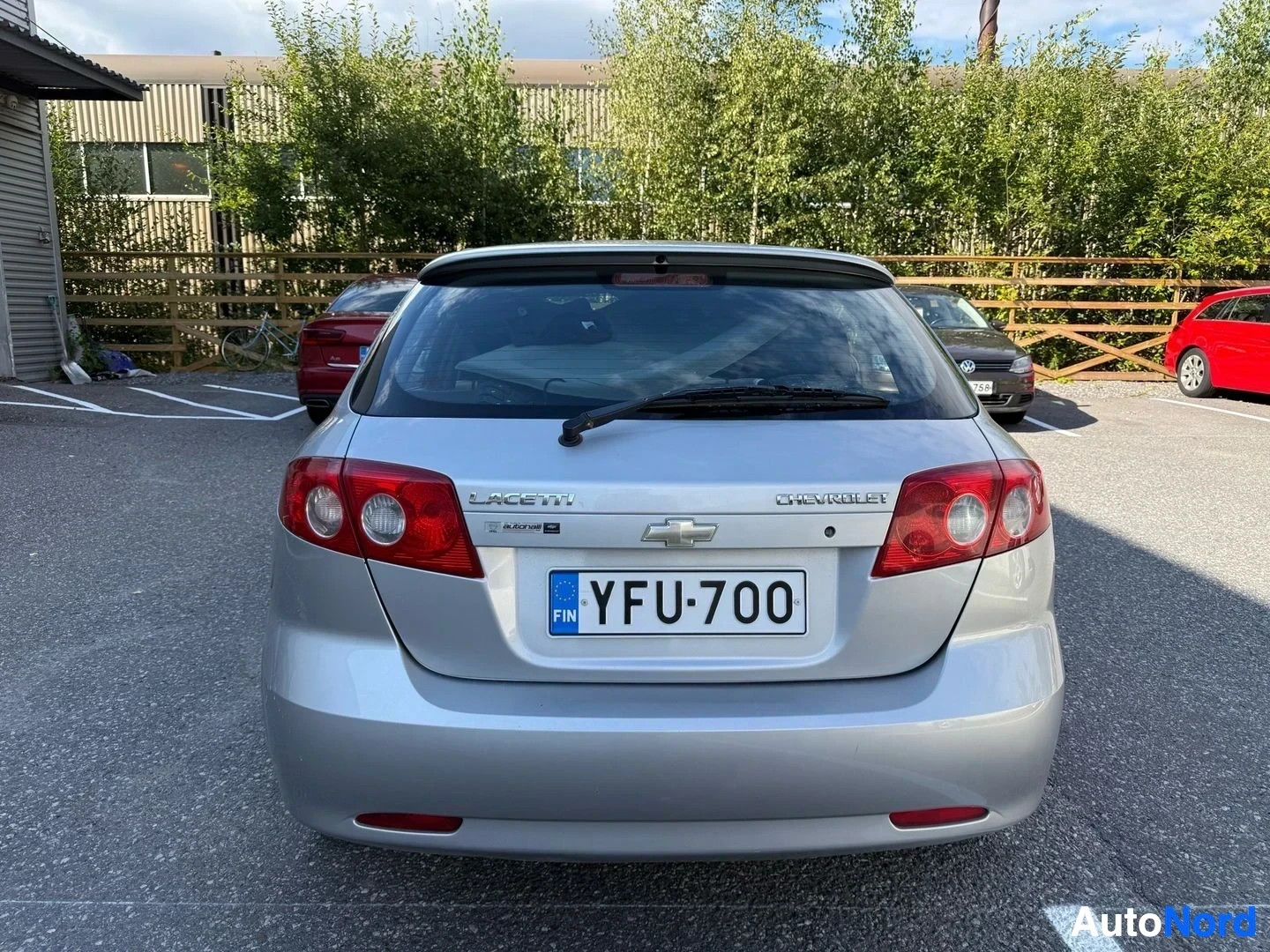 Takaa: Hopea Chevrolet Lacetti sedan takaa, rekisterikilpi näkyvissä, punaiset takavaloproteiinit, pysäköintialueella