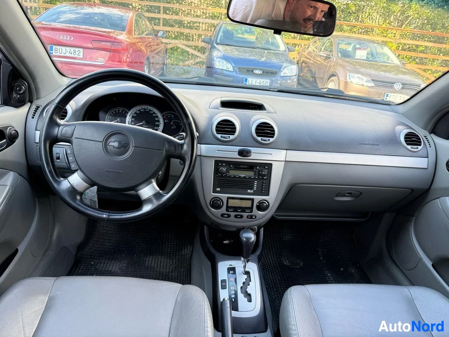 Ohjaamo: Auton sisäkuva, musta monikäyttöinen ohjauspyörä Chevrolet-logolla, instrumenttilautapaneeli, radio, valkoinen istuinverhoilu, automaattivaihteisto