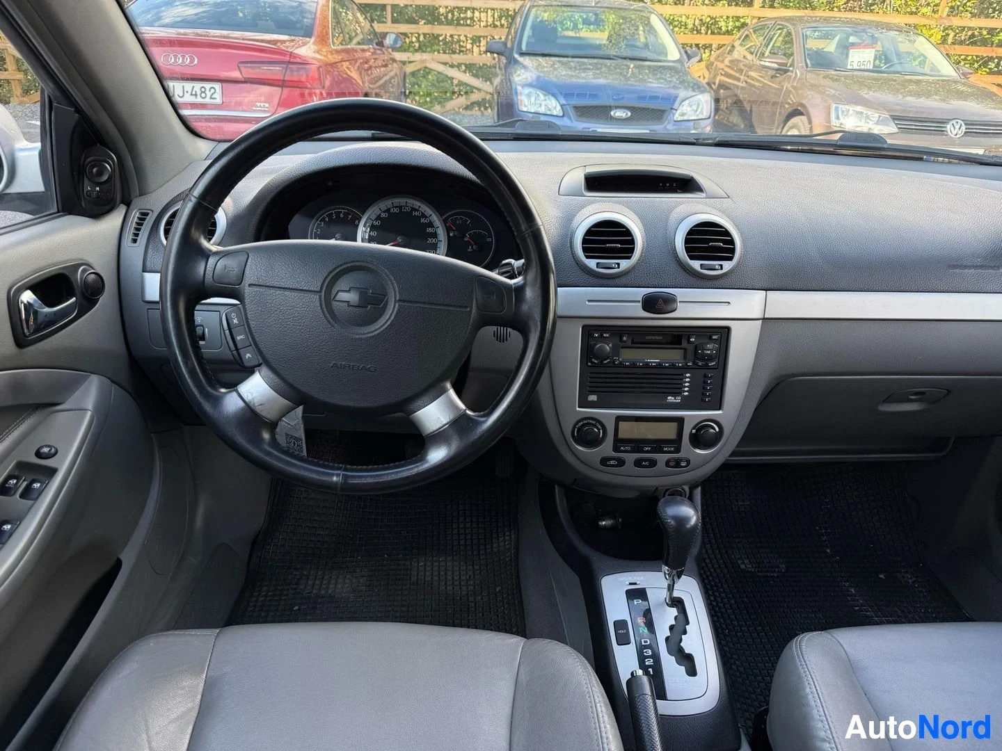 Ohjaamo: Auton kuljettajan paikka sisältä kuvattuna. Näkyy musta vääntöpyörä Chevrolet-logolla, instrumenttinäyttö, ilmastoinnin säädöt, radio/cd-soitin ja valkoiset ist