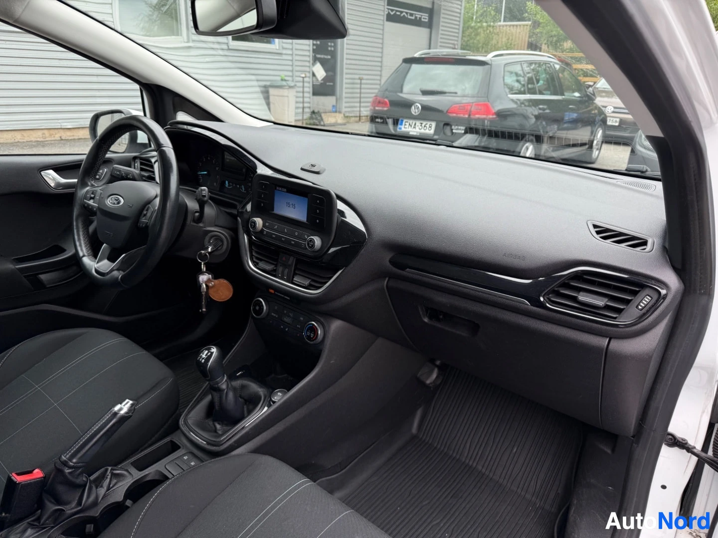 Etuistuimet: Ford Fiestan kuljettajan puoli sisätila, näkyy rata, sininen näyttö kojelaudalla aika 15:16, musta istuin, harmaa kojelauta