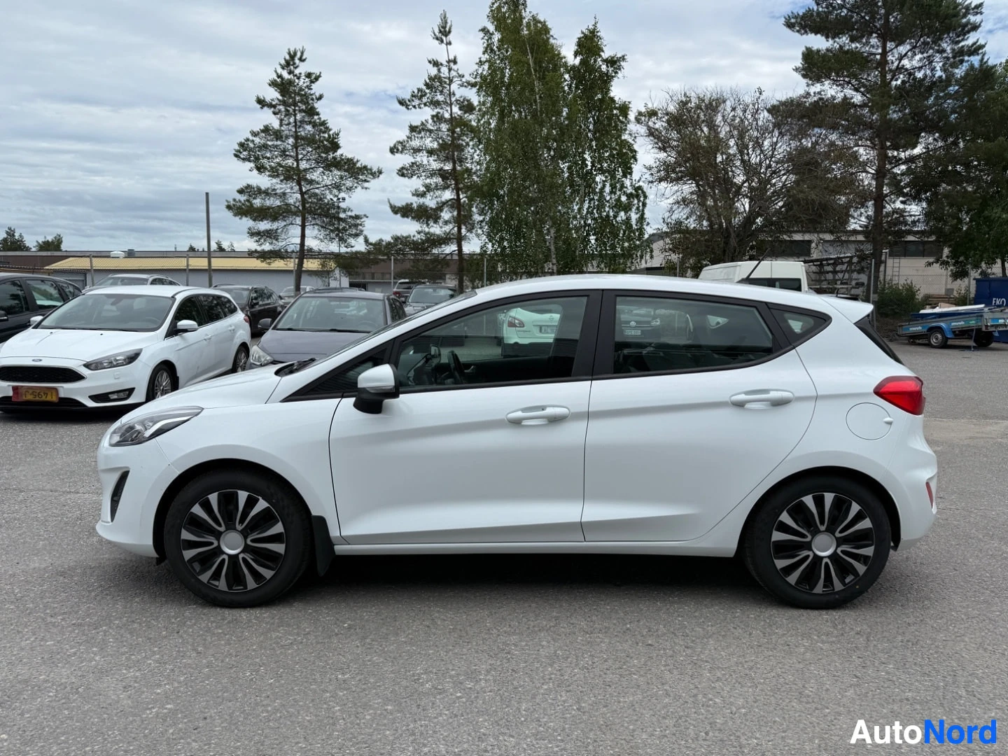 Sivulta: Valkoinen Ford Fiesta sivusta katsottuna vasemmalle päin, alumiiniset pojat näkyvissä, neliksi ovi avoin