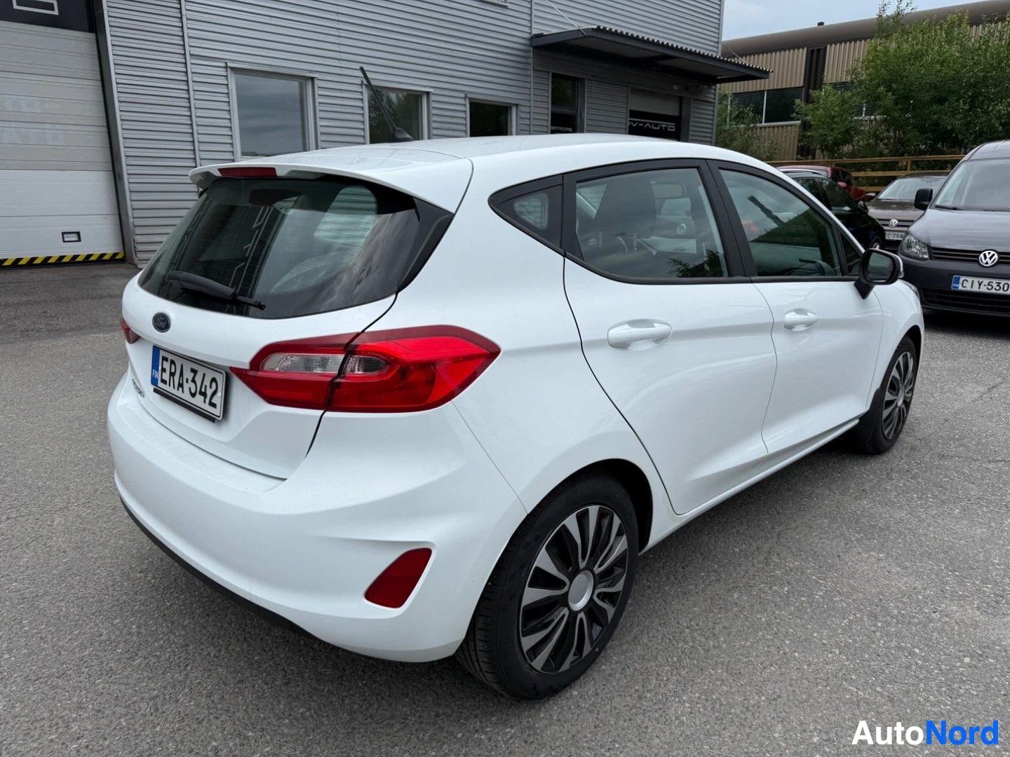 Takaviisto: Valkoinen Ford Fiesta takaa sivulta näkymä punaisten takavalojen ja rekisterikilven kanssa.