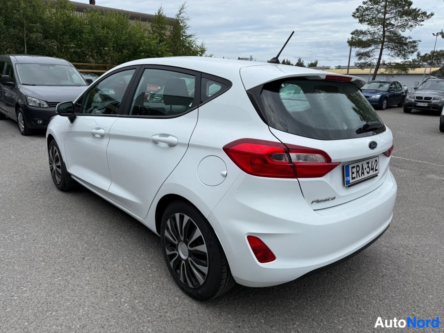 Takaviisto: Valkoinen Ford Fiesta kolmen neljänneksen näkymässä oikealla puolella, ovi auki, alumiiniset pojat näkyvissä