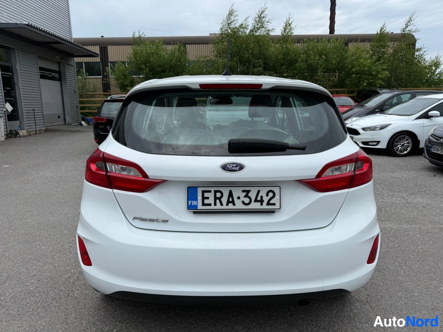 Takaa: Valkoinen Ford Fiesta takaapäin katsottuna, rekisterinumero, punaisten takavalojen ja valkoisen rungon näkyvissä