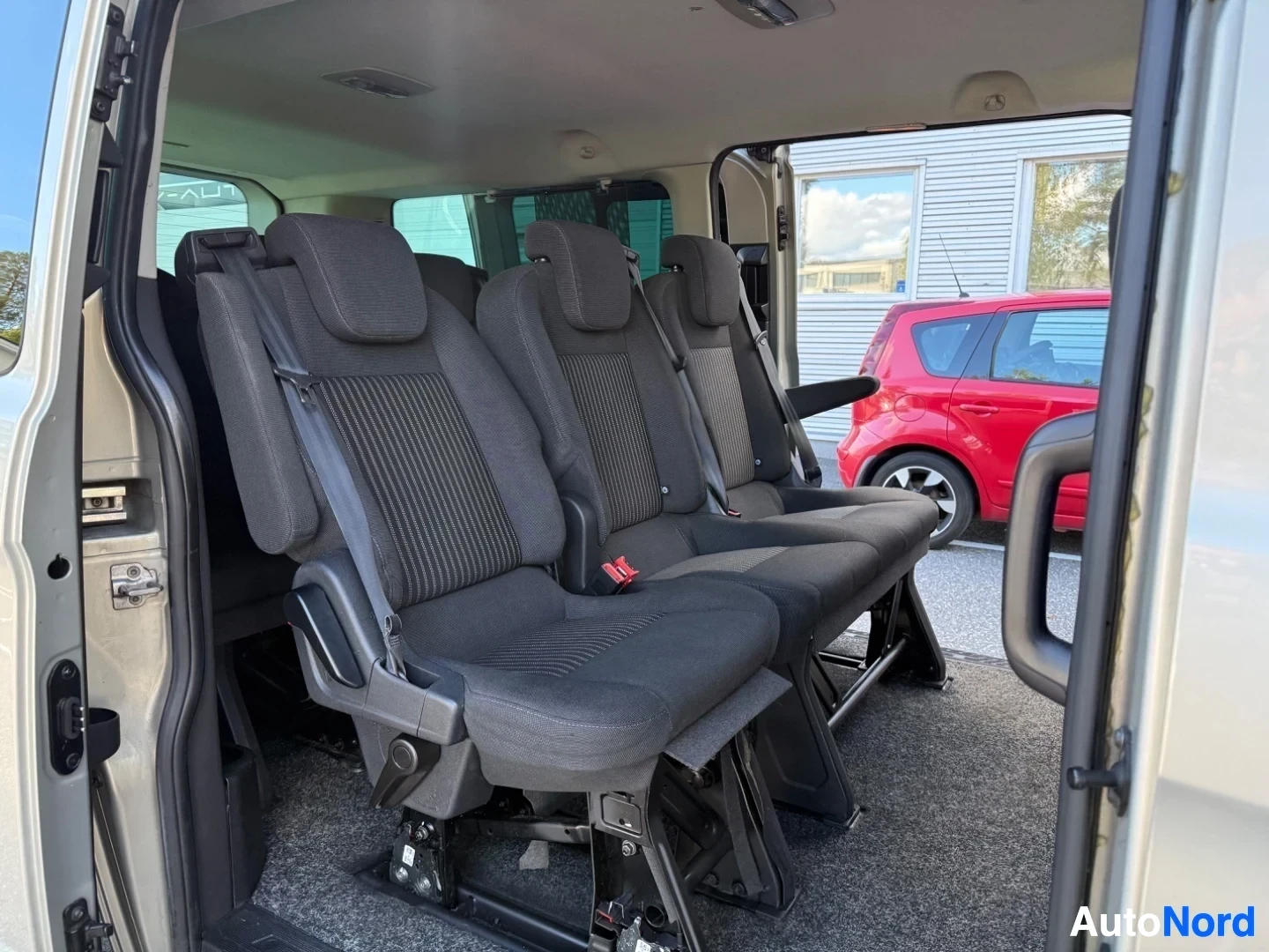 Ohjaamo: Väljä matkustajakupla, joissa mustia istuimia ja turvavöitä. Oikeanpuoleinen ovi avoin. Taustalla punainen auto ja siilorakennuksia.
