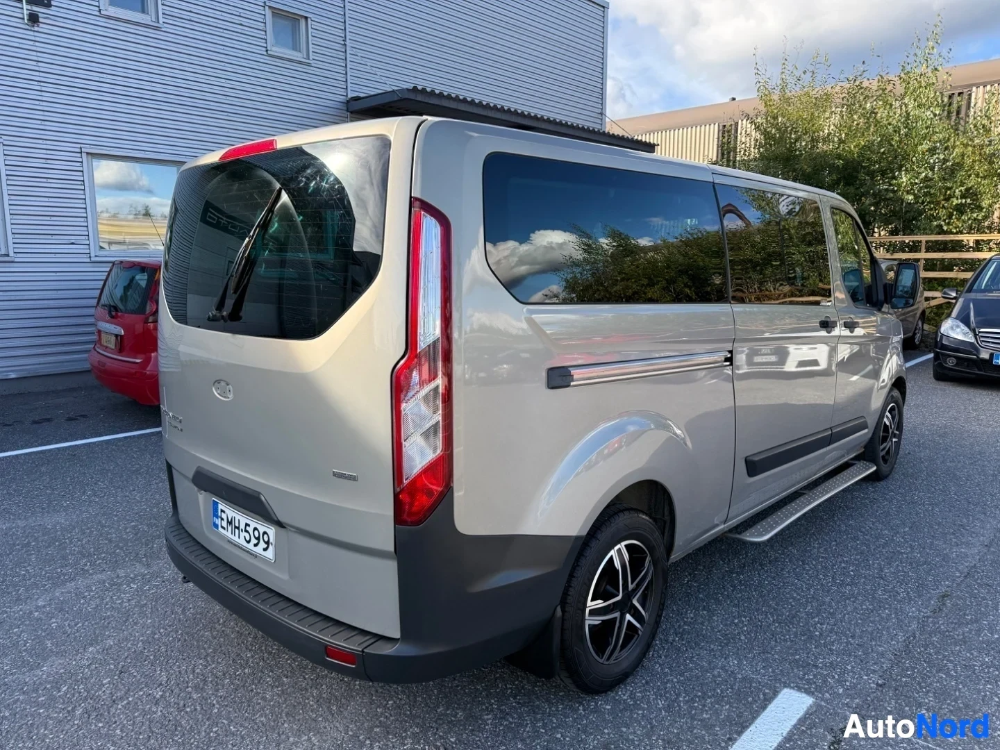 Takaviisto: Valkoinen Ford Tourneo Custom -pakettiauto takakolmen neljänneksen kulmasta oikealta vasemmalle, takalamppu punaisena näkyvissä