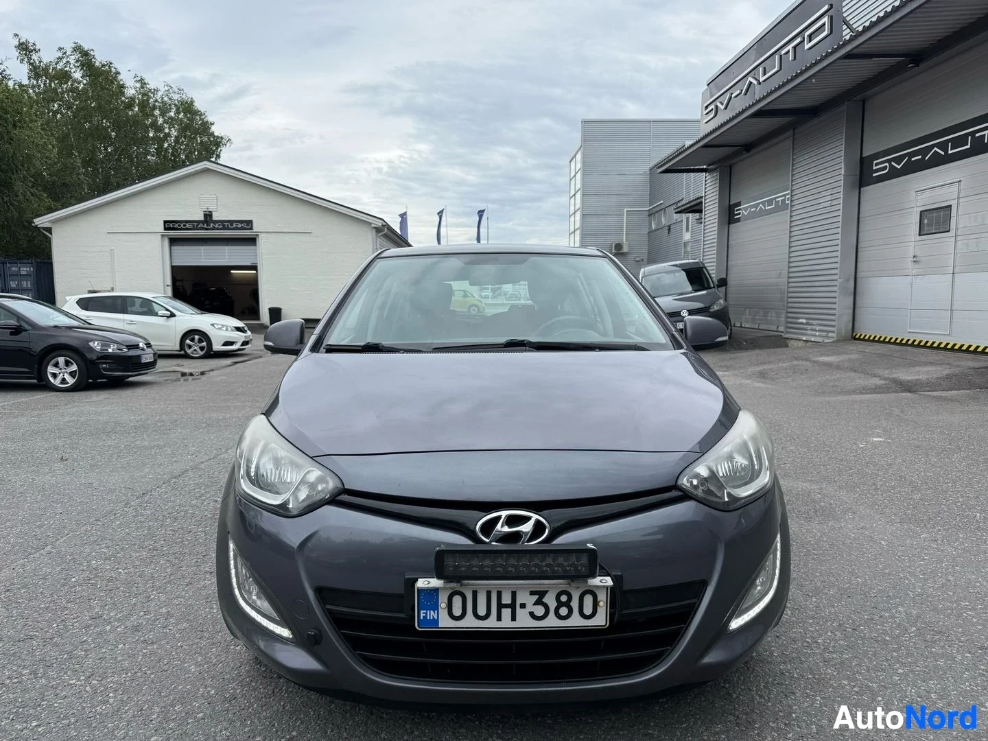 Edestä: Harmaa Hyundai i20 etulta nähtynä, rekisteritunnuksella, korjaamisen edessä