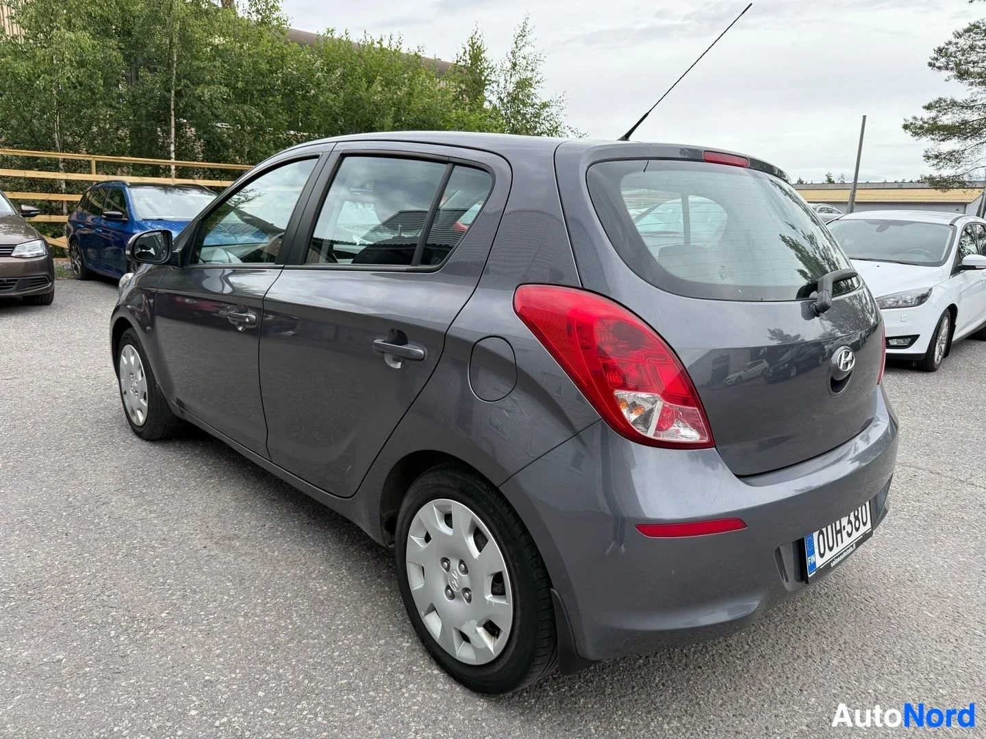 Sivulta: Harmaa Hyundai i20 vasemmalta sivulta, ovi avattuna ja valkoiset vanteet näkyvissä.