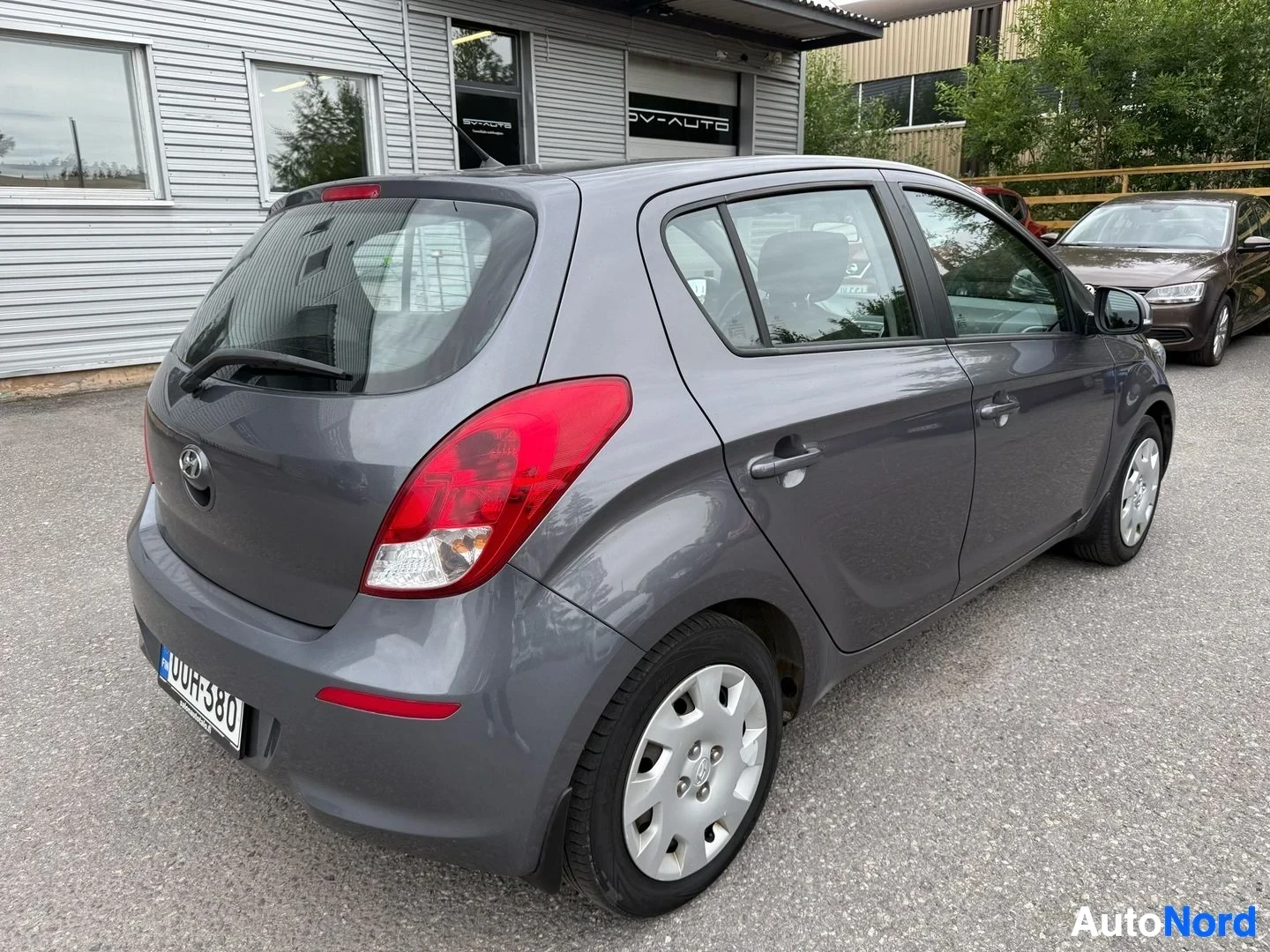 Takaviisto: Harmaa Hyundai i20 takaa kolmen neljäsosan kulmasta, ovet auki, punainen takalämpö näkyy