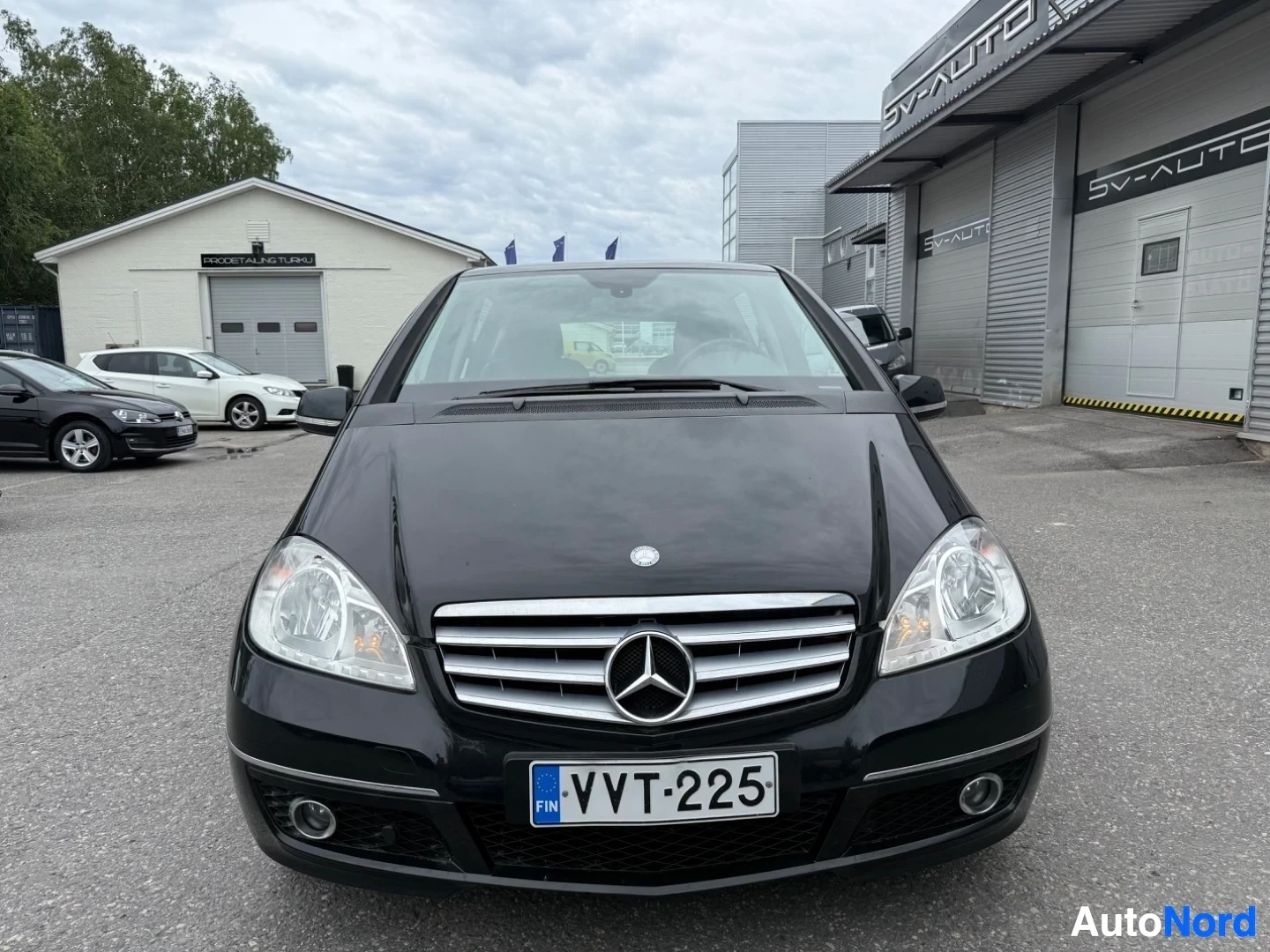Edestä: Musta Mercedes-Benz A160 etukuva pysäköintialueella, näkyvät sumuvalaisimet ja Chrome-grilli