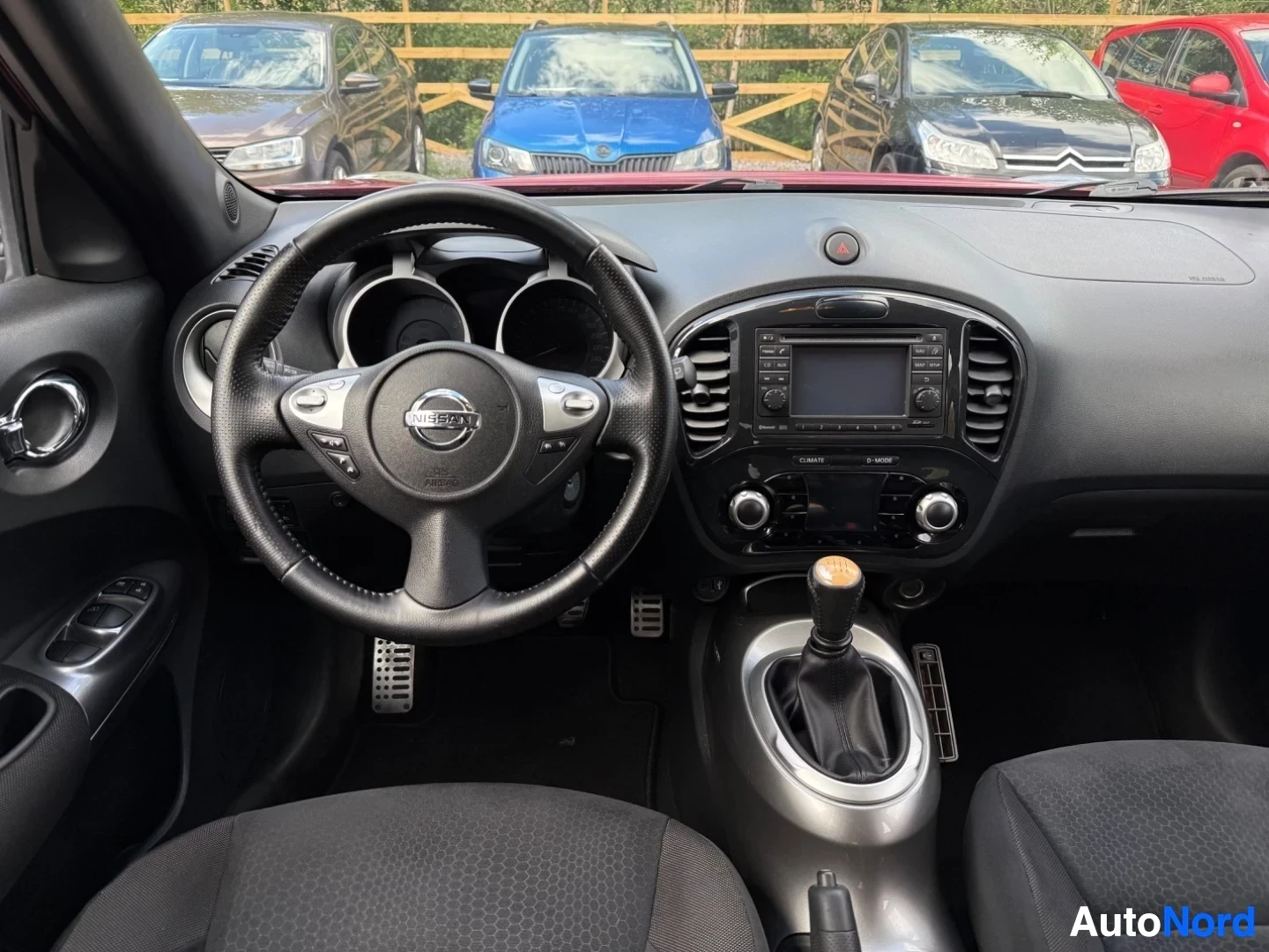 Etuistuimet: Juken ohjauspyörä Nissan-logolla, infotainment-näyttö, ohjattava puoli vasemmalla, auton sisätila kuljettajan perspektiivistä