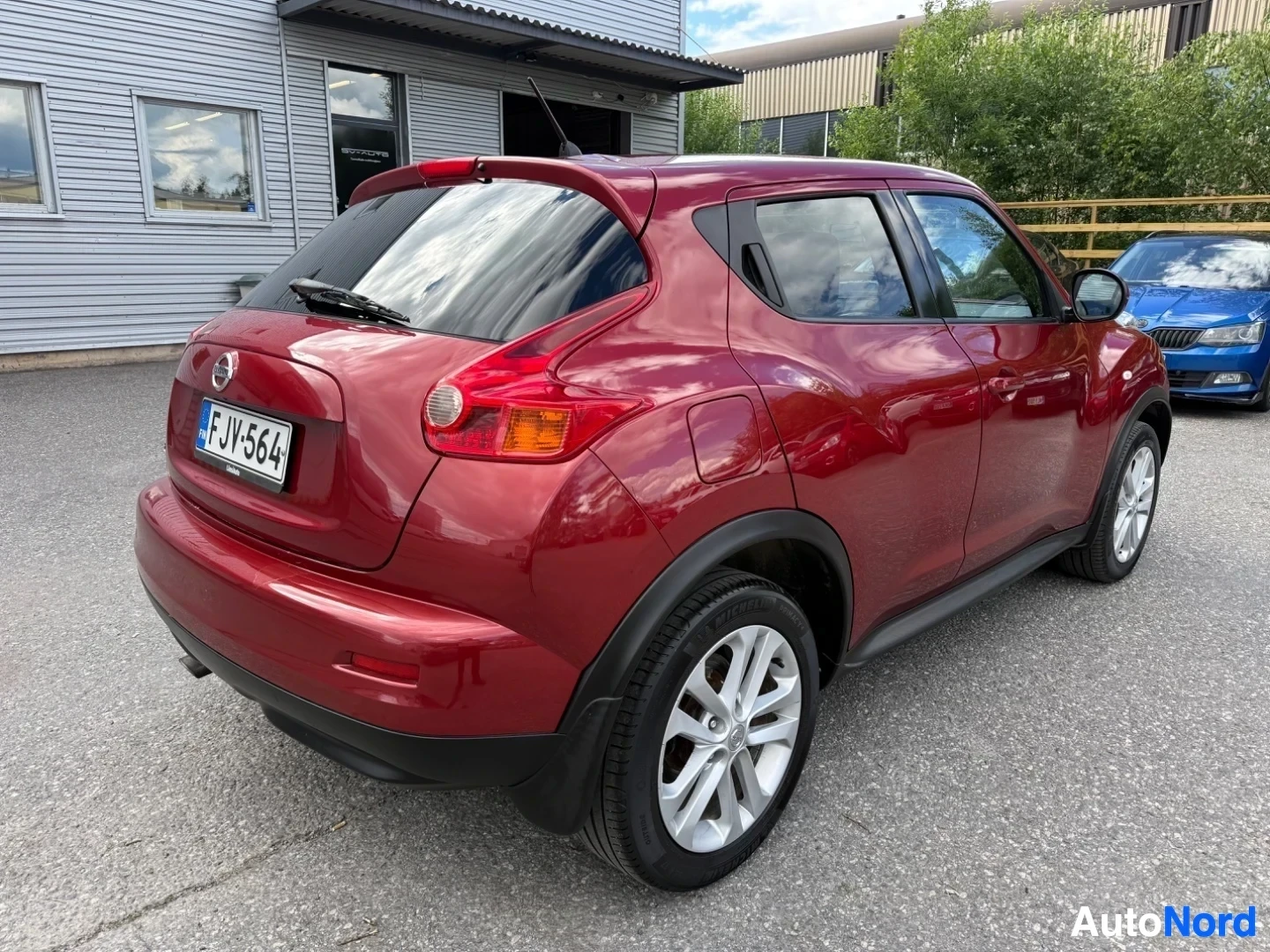 Takaviisto: Punainen Nissan Juke, kuvattu takaa kolmen neljänneksen kulmasta oikealta. Näkyvissä taka-osa, oikea sivu ja osa vasemmasta sivusta. Valkoisen kehyksen pyörät.