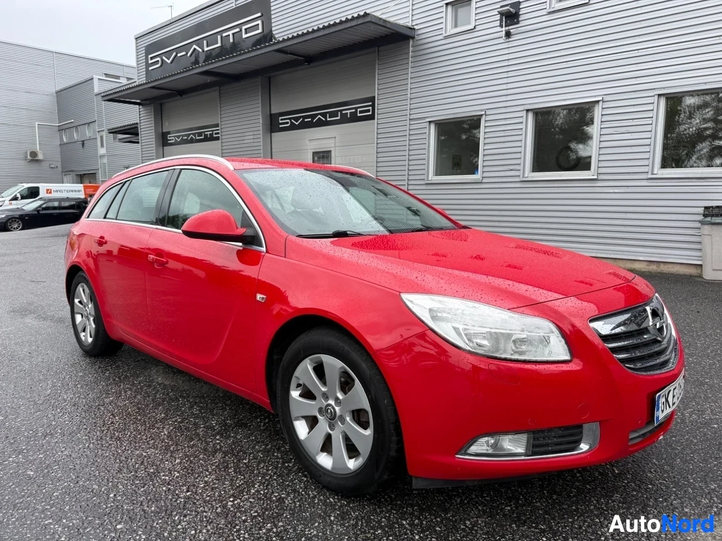 Etuviisto, nokka oikealle: Punainen Opel Insignia Sports Tourer, kuvattu kolmelta sivulta etuosasta oikealle, pysäköitynä myyntiliikkeen edustalla.