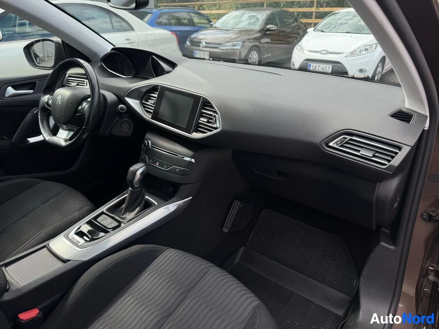Etuistuimet: Auton sisätila oikealta puolelta: Peugeot-ratti, kosketusnäyttö keskikonsolin yläosassa, ilmastointiaukkoja, harmaat kangaspäällysteiset istuimet, harmaa sisust