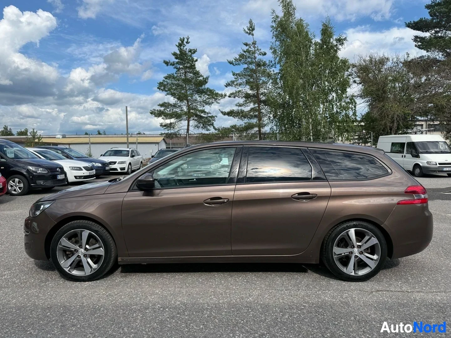 Sivulta: Ruskea Peugeot 308 SW pysäköinti-alueella, oikealta sivulta, pitkä vartalo, neljä ovea, hopeanväriset vanteet, pysäköintihallissa.