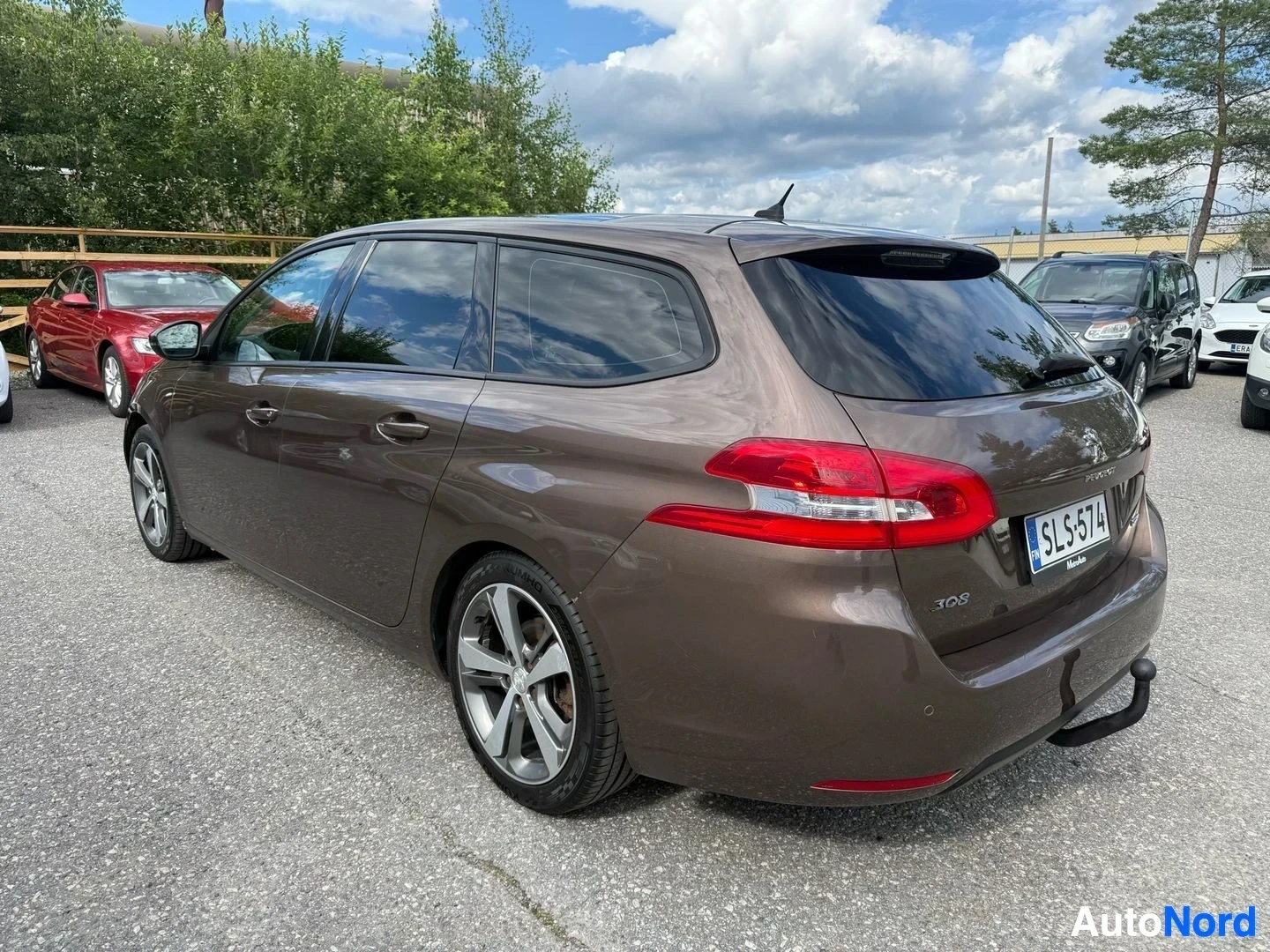 Sivulta: Ruskea Peugeot 308 SW oikealta sivulta, neljä ovea näkyvissä, hopeanväriset vanteet, rekisterikilpi, punainen takavalasin, pysäköintihallin paikalla
