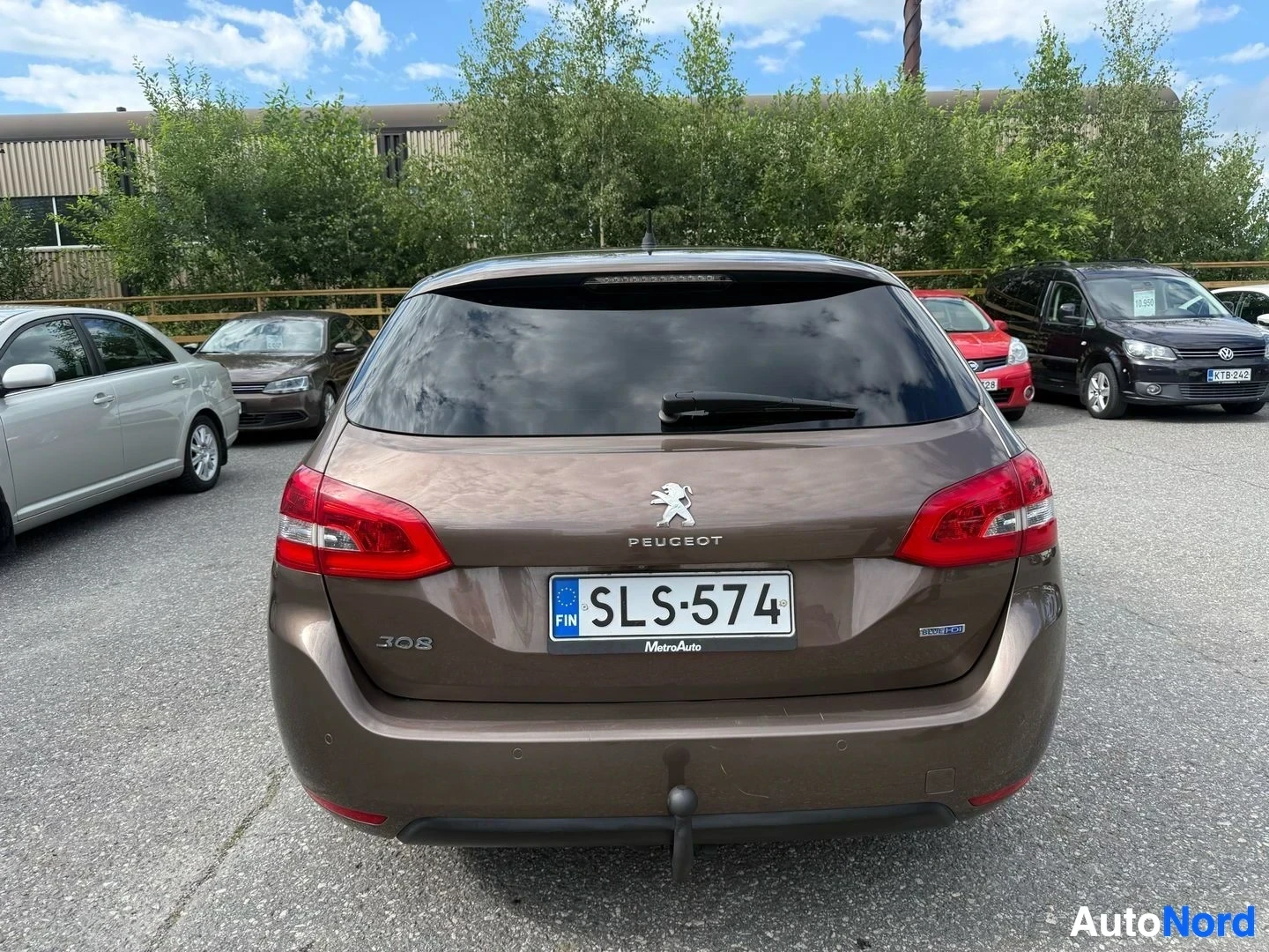 Takaa: Ruskea Peugeot 308 SW takaapäin pysäköintihallin parkkipaikalla, rekisterikilpi näkyvissä, punaiset takavalaisimet, valkea Peugeot-tunnus takaovet