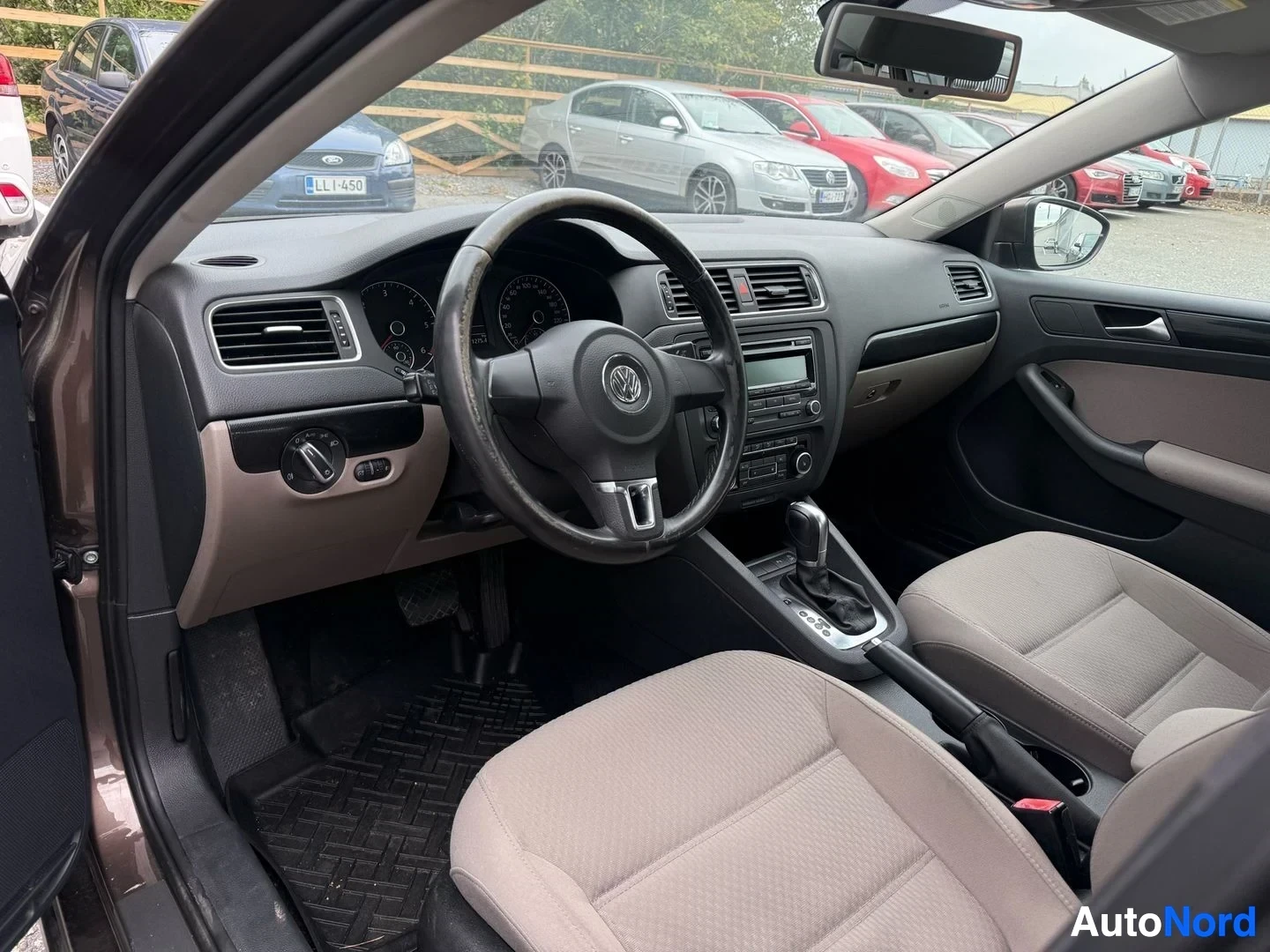Etuistuimet: Volkswagen-merkkisen auton ohjamo, näkymä kuljettajan puolelta. Näkyy kaksiväri-istuin (beige ja musta), ohjauspyörä Volkswagen-logolla, ilmastointi-ohjaimet, n