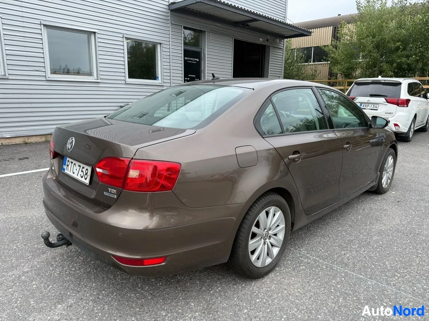 Takaviisto: Ruskea Volkswagen Jetta takaosasta katsoen, avautuva ovi, punaiset takavalaisimet näkyvissä.
