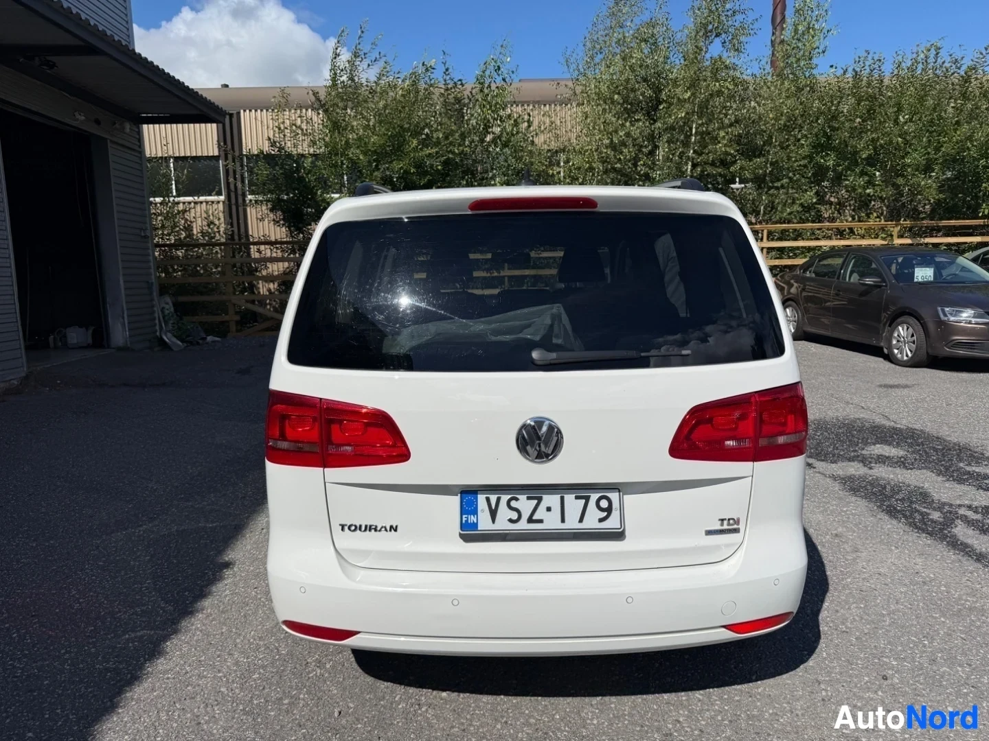 Takaa: Valkoinen ja punainen Volkswagen Touran takaa, punaisten takavalojen näkyvästi, rekisterikilpi VS-179, TDI-merkintä takaosuudessa.