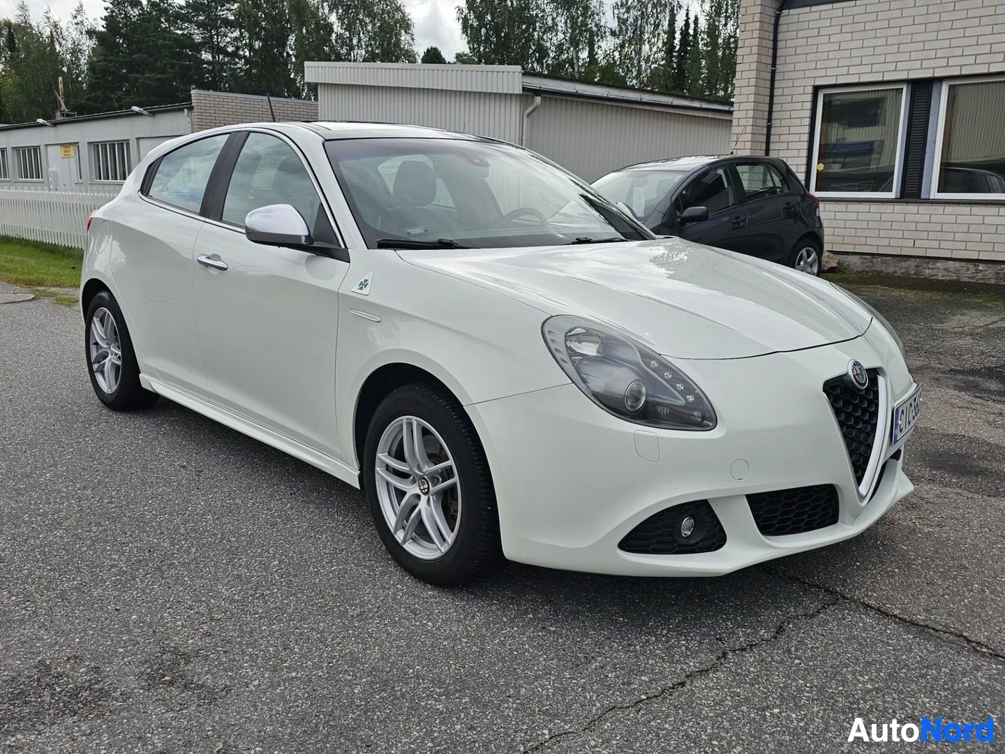 Etuviisto, nokka oikealle: Valkoinen Alfa Romeo Giulietta kolmioven hatchback, kuvattuna vasemmalta kolmipuolelta pysäköintialueella.