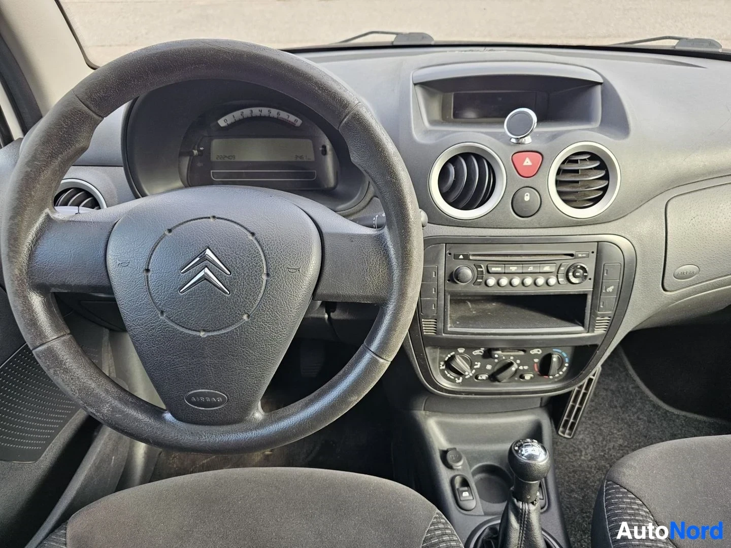 Yksityiskohta: Lähikuva kojelaudasta ja ohjauspyörästä, Citroën-logo ohjauspyörässä näkyy, radio ja ilmastointi-ohjaimet.