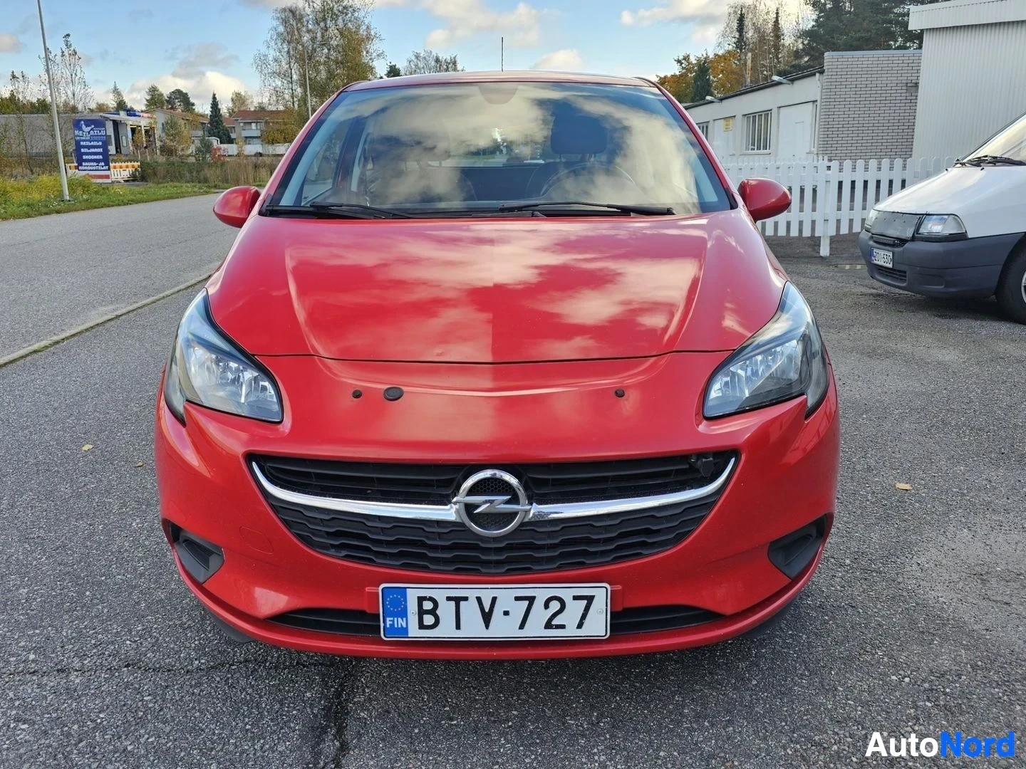 Edestä: Punainen Opel-auto kuvattuna suoraan edestä pysäköintipaikalla, rekisterikilpi näkyvissä