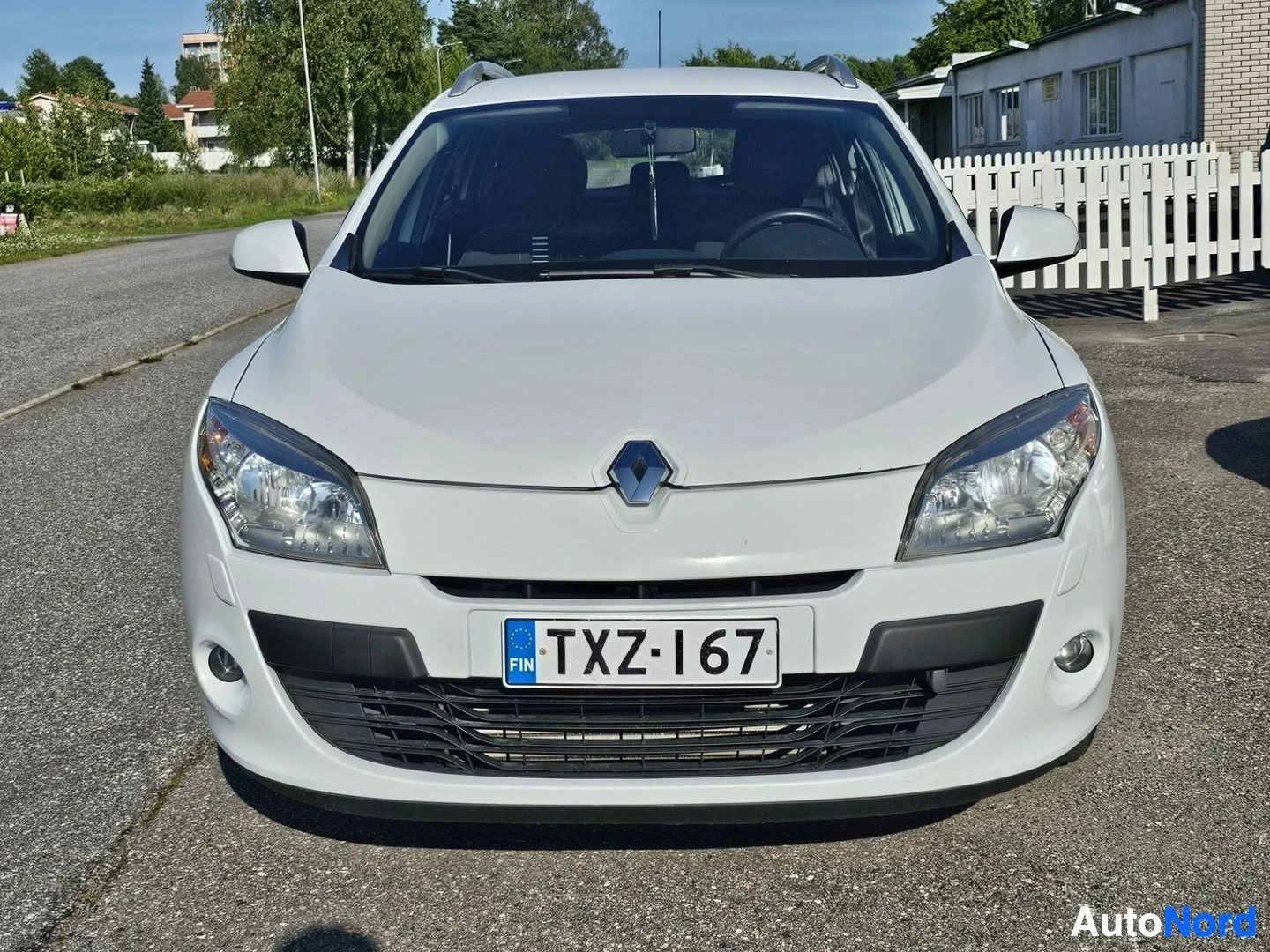 Edestä: Valkoinen Renault Megane Sport Tourer -farmari edestä kuvattuna. Näkyvät LED-päiväajovalot, Renault-tunnus grillissä ja rekisterikylpi