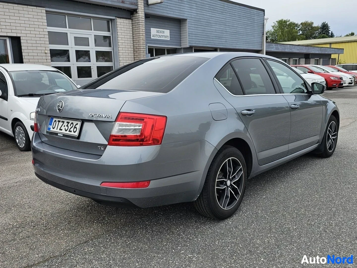 Takaviisto: Harmaa Skoda Octavia takaviistosta oikea puoli, ovi auki, punainen takavalo, alumiiniset vanteet, 'OCTAVIA' teksti takaisussa