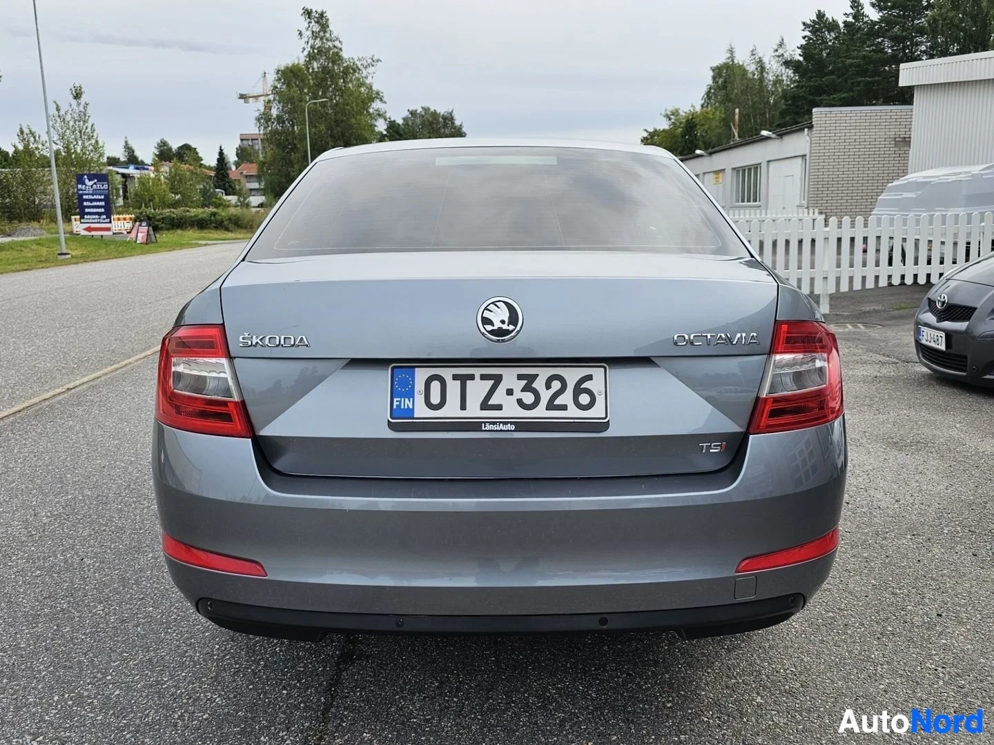 Takaa: Harmaa Skoda Octavia takaa kuvattuna, teksti 'SKODA OCTAVIA TS' näkyvillä takaluukulla, punainen takavalo, rekisterikilpi