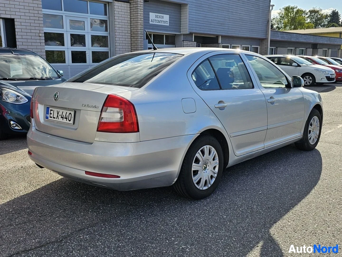 Takaviisto: Hopeanvärinen neliovi sedan, kuvauspaikalla autoliike. Auto näkyy takapuolelta kolmen neljänneksen kulmasta oikealle osoittavan nenän kanssa. Rekisterikilvessa