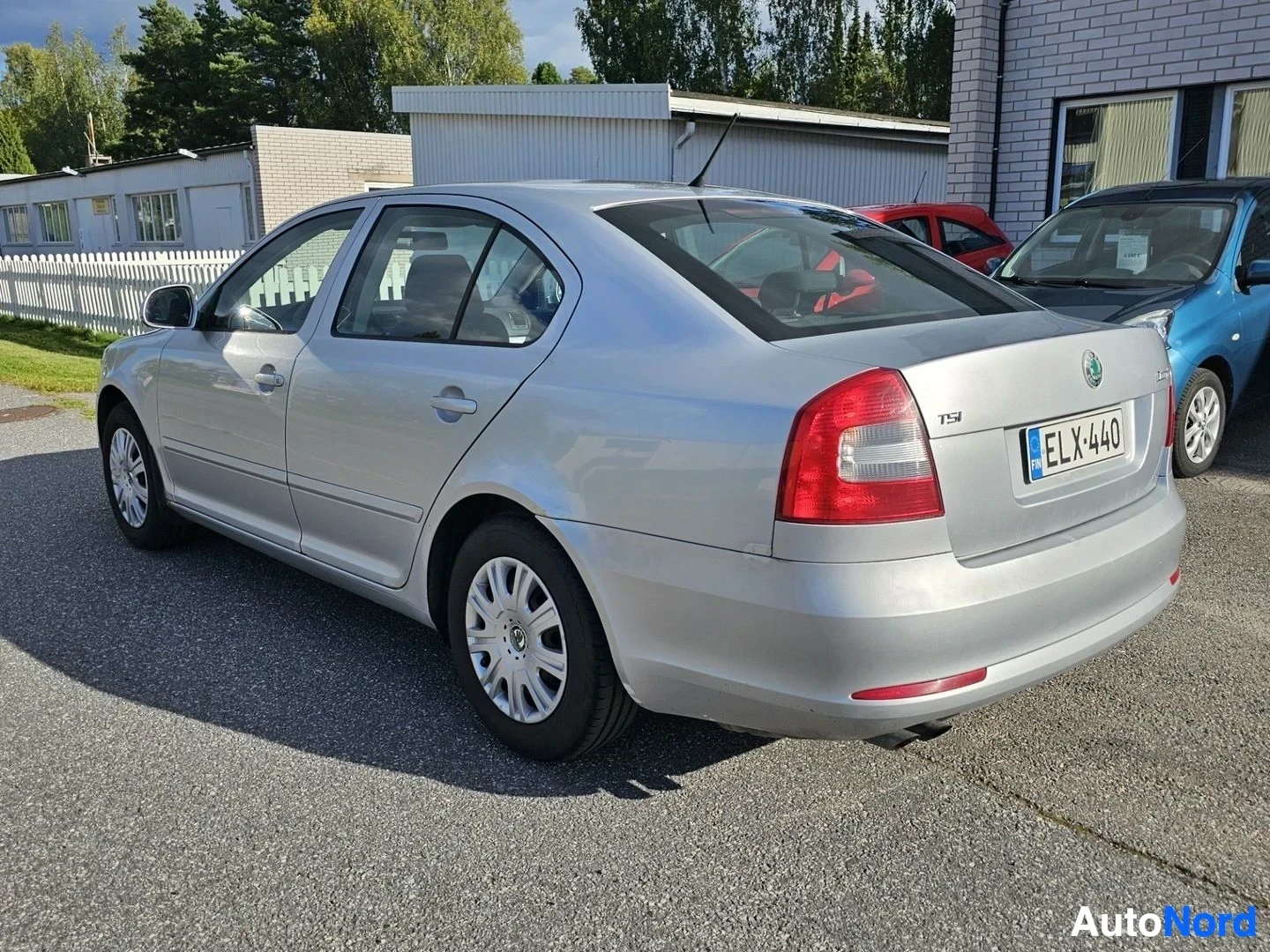 Takaviisto: Hopeanvärinen neliovi sedan, kuvauspaikalla autoliike. Auto näkyy taaksepäin osoittavan nenän kanssa etupuolelta kolmen neljänneksen kulmasta. Rekisterikilvessa
