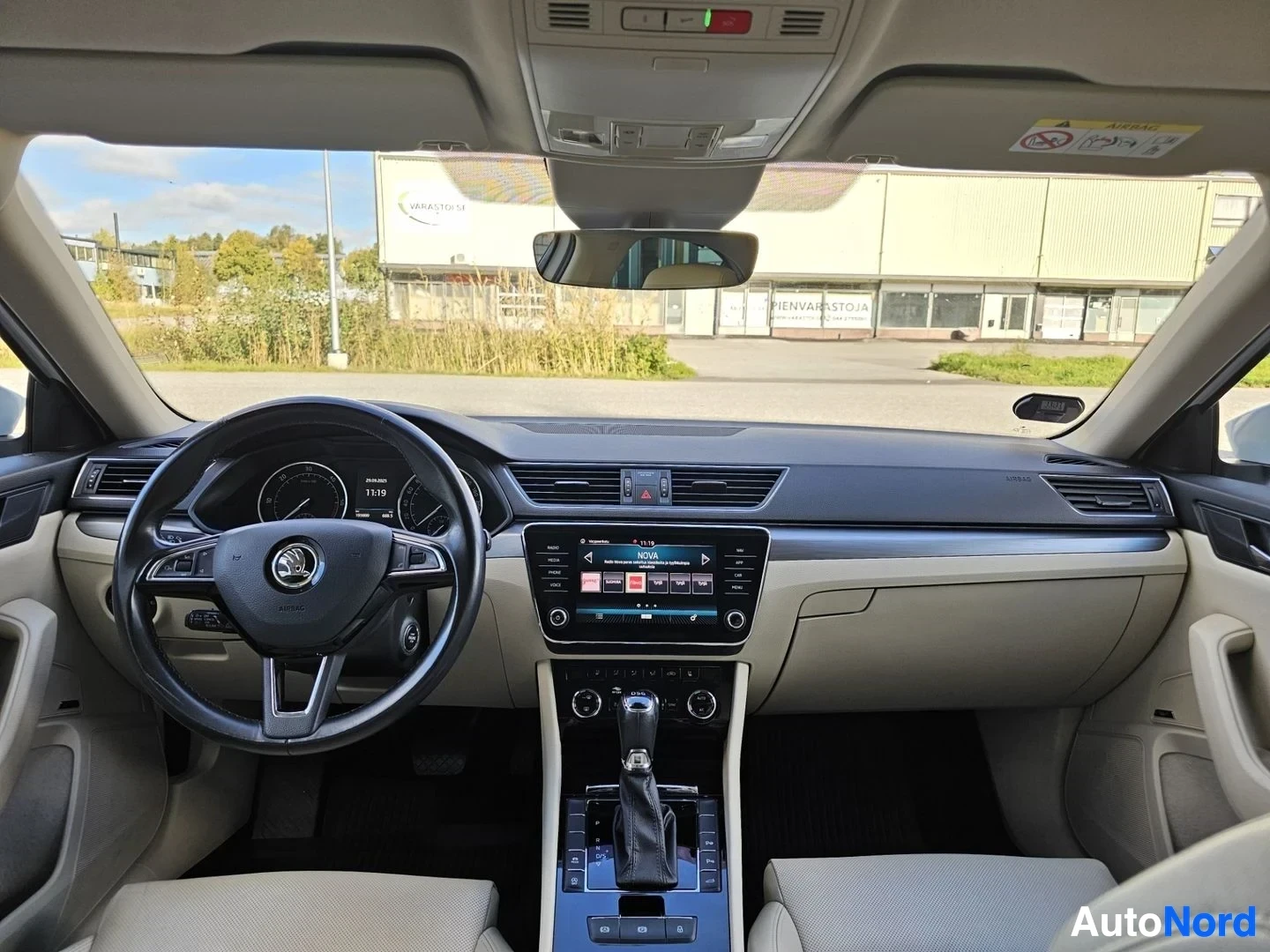 Ohjaamo: Auton ohjaamo edestä katsottuna: Skoda-logo ohjauspyörässä, kosketusnäyttö keskikonsolissa, vaaleat istuimet, kattovalaistus ja tuulilasi