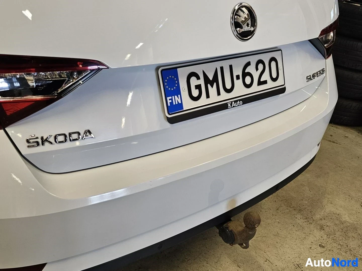 Takaa: Valkoisen Skoda Superbin takalokasuoja ja rekisterilevy, näkyvissä 'SKODA' merkki ja 'SUPERB' teksti