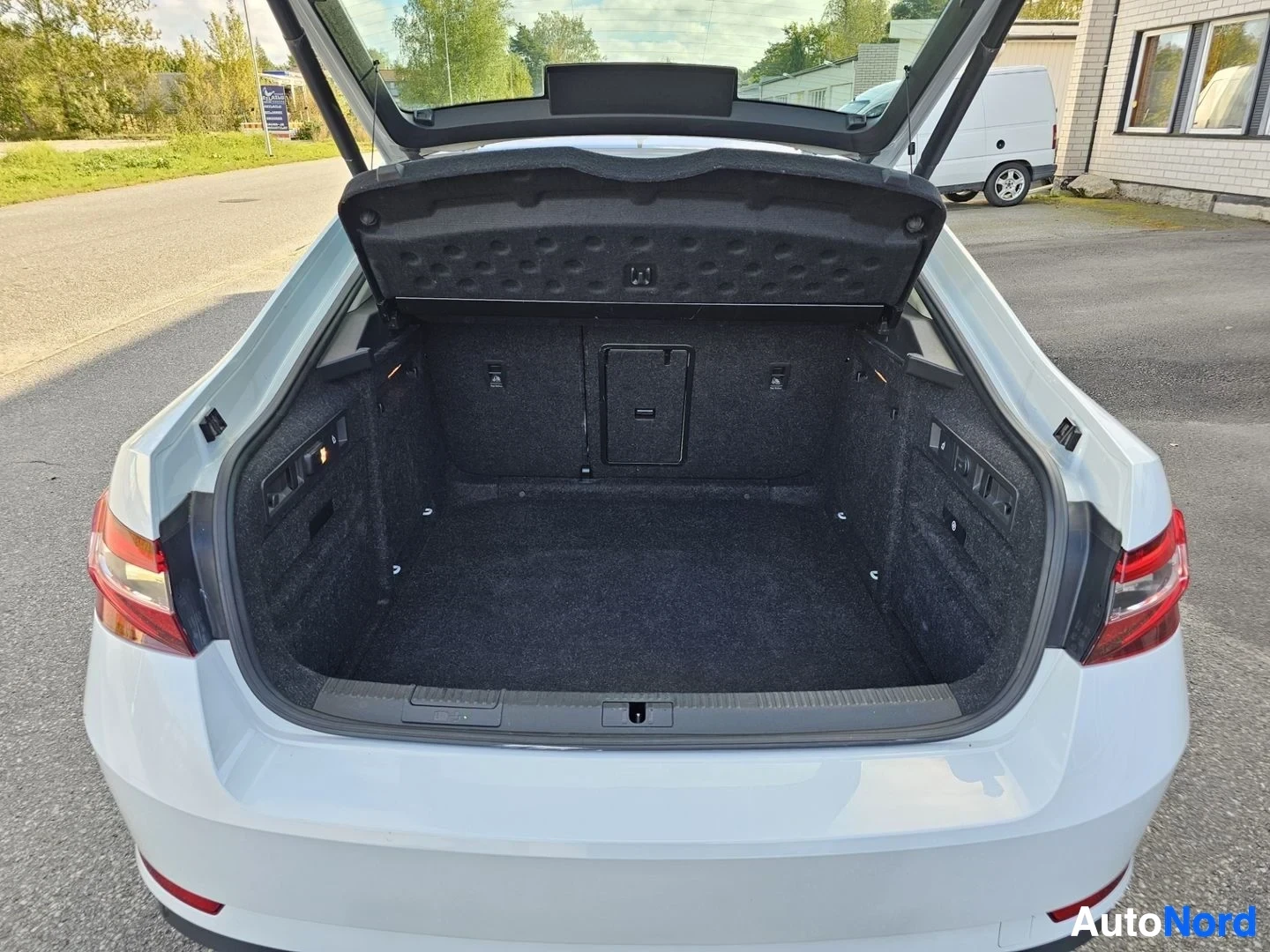 Tavaratila: Valkoisen Skoda Superbin auki avattu takaluukku, mustalla villa-matolla päällystetty lastin alue, näkyvissä sähköisen liitäntälaitteen kanava