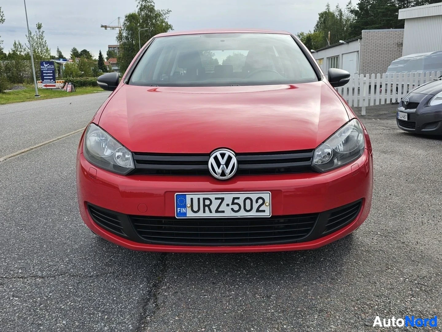 Edestä: Punainen Volkswagen Golf etulta, rekisterinumero näkyvissä, pysäköitynä asfalttialueelle