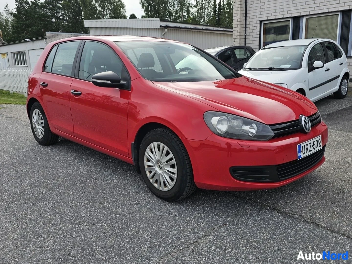 Sivulta: Punainen Volkswagen Golf sivulta, näkyvissä neljä ovea ja valkoiset vanteet, rekisterinumero